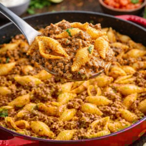 Cheesy Taco Pasta Shells in a red pan with a spoon lifting up a bite