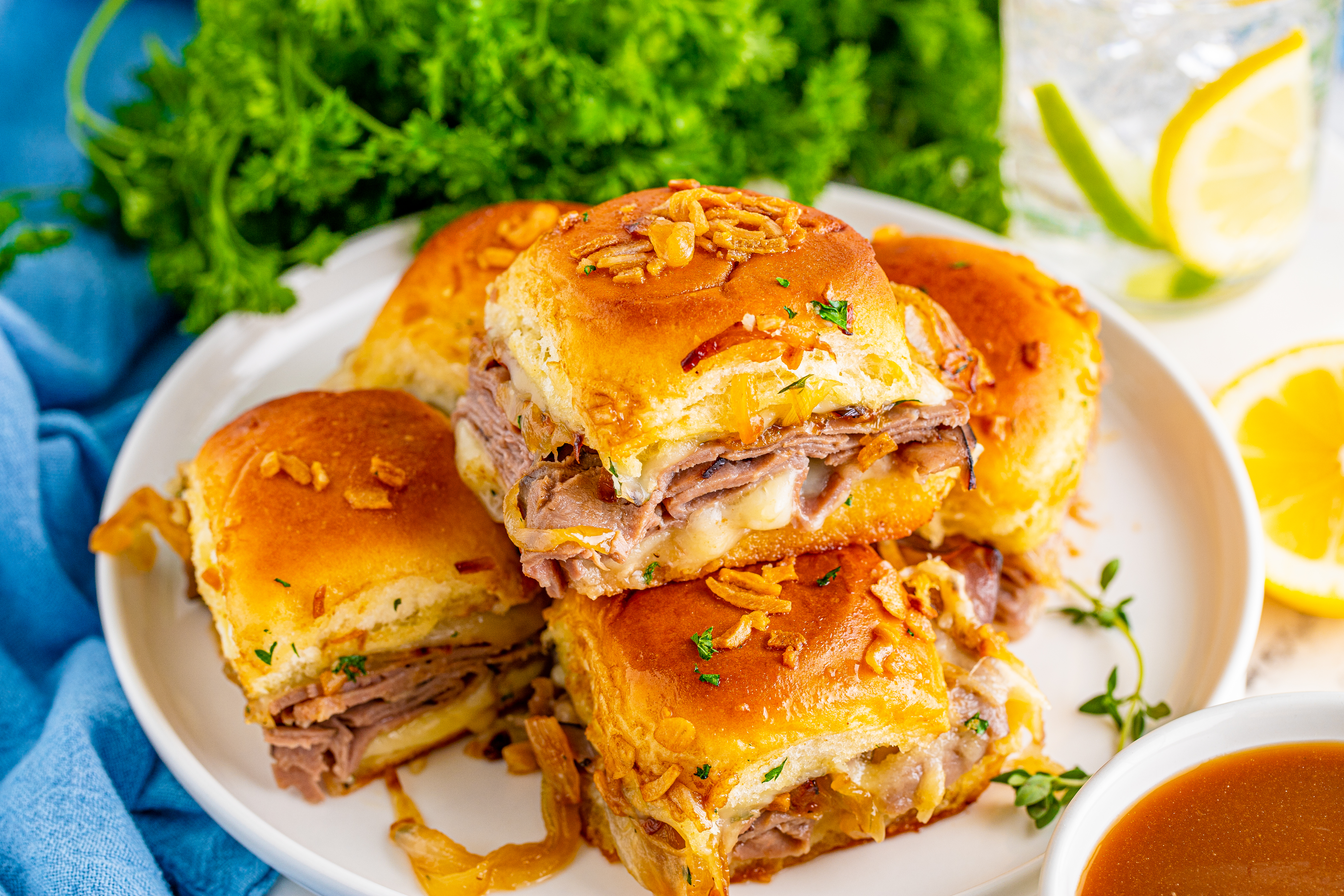 French Dip Sliders piled on a white plate with a blue napkin