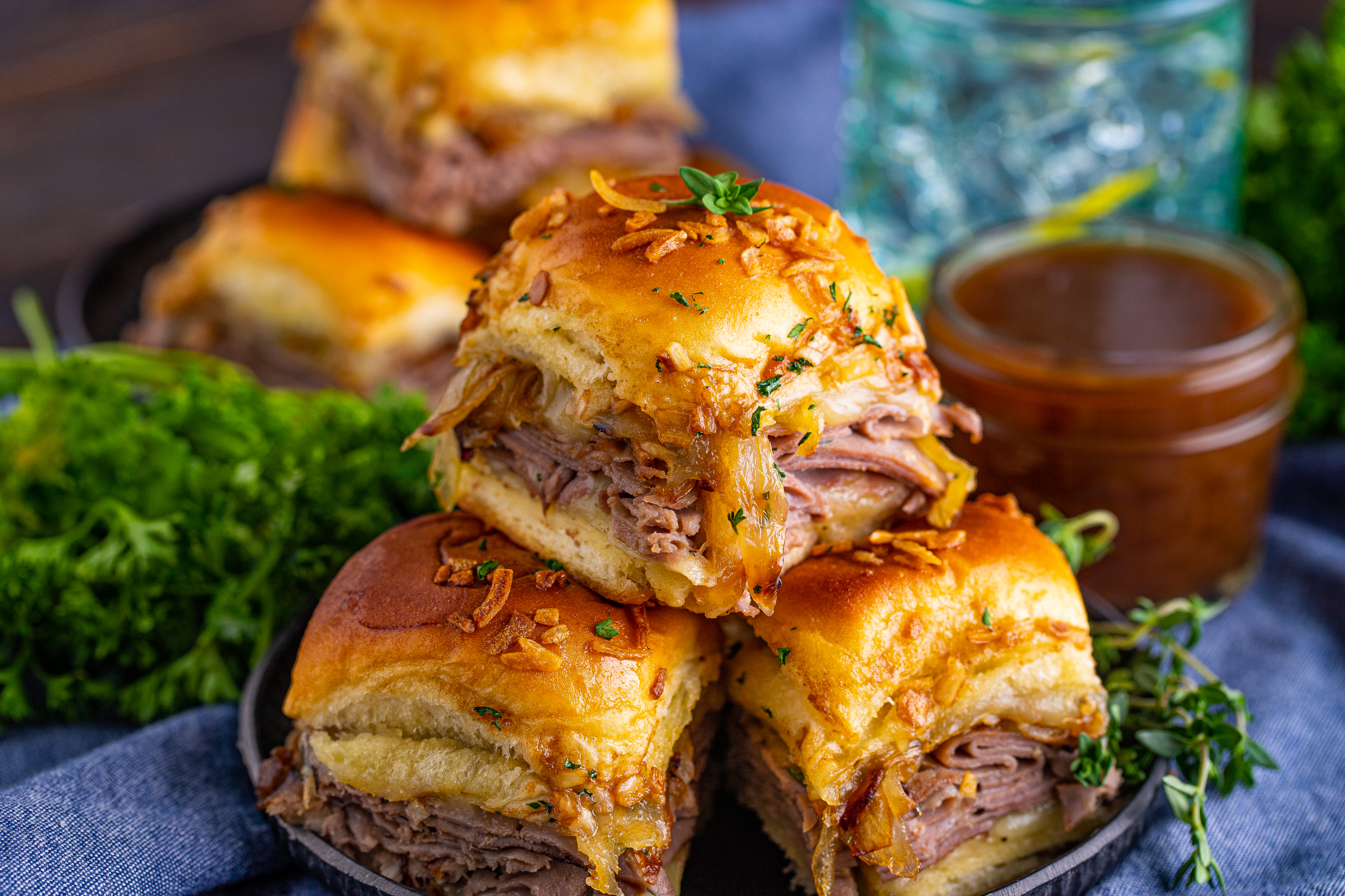 Three French Dip Sliders piled on a black plate with a container of au jus next to it