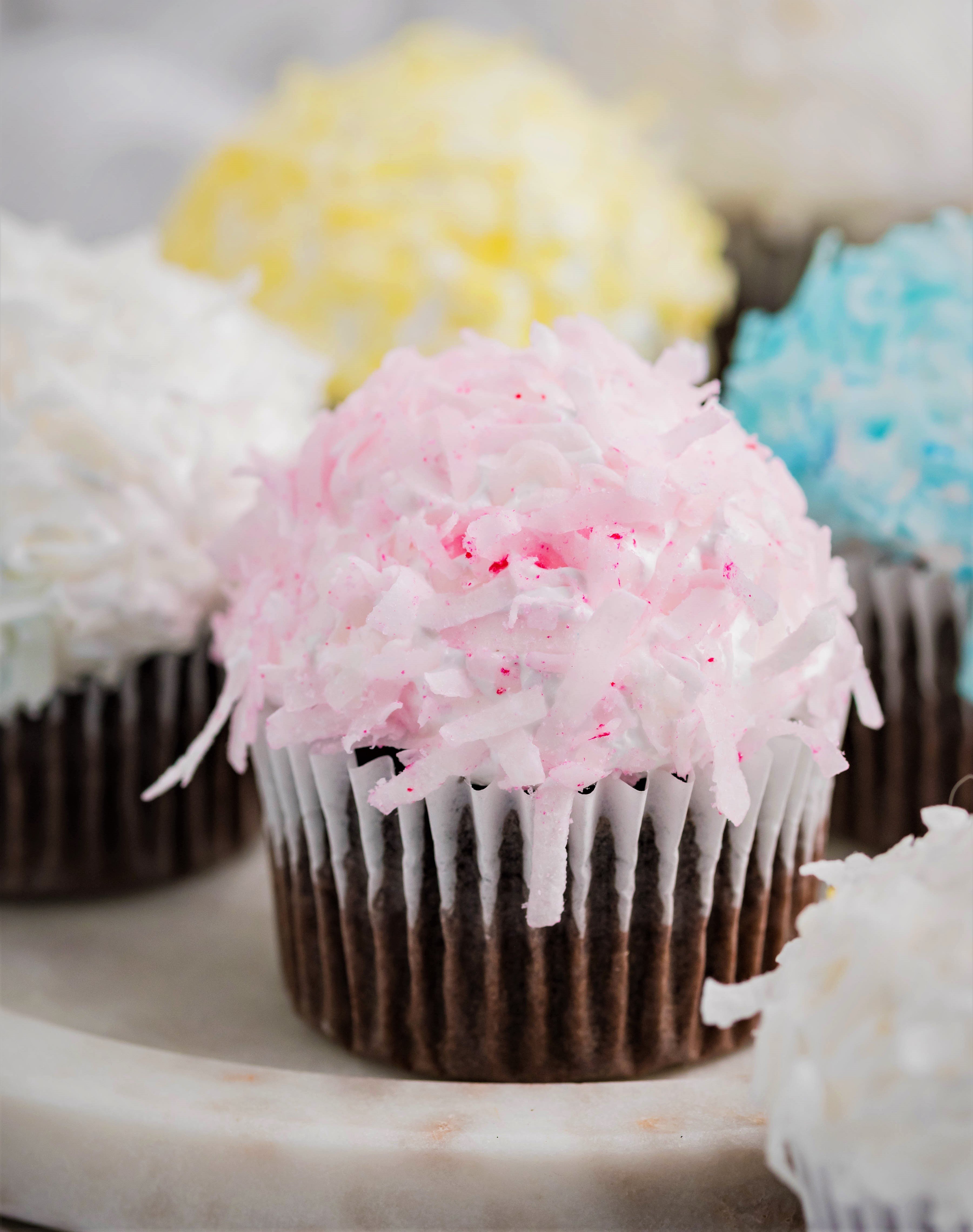 chocolate cupcakes that are Pink, yellow, white and blue topped with coconut