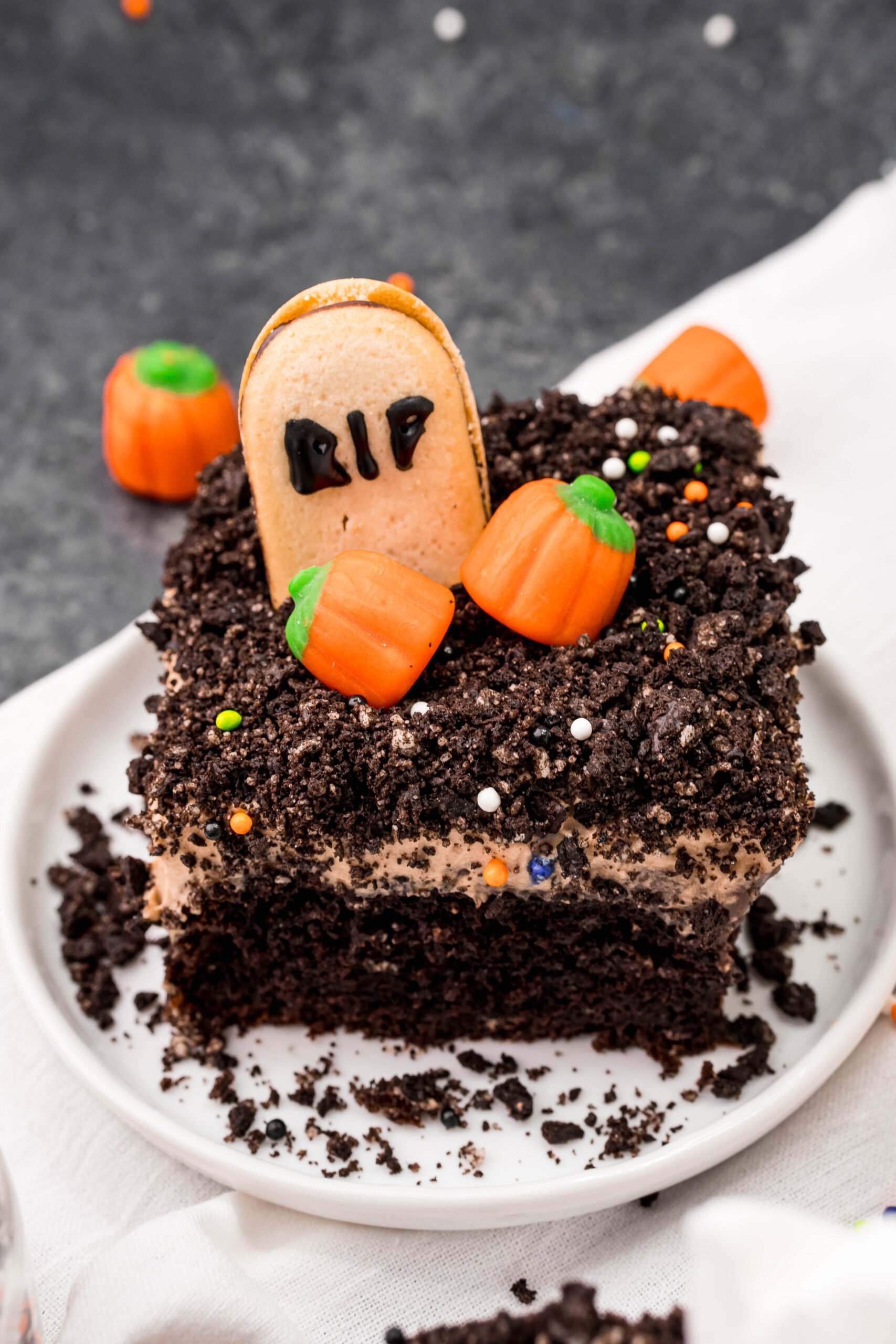 Halloween Dirt Cake slice on a white plate with oreo crumbles and mini candy pumpkins