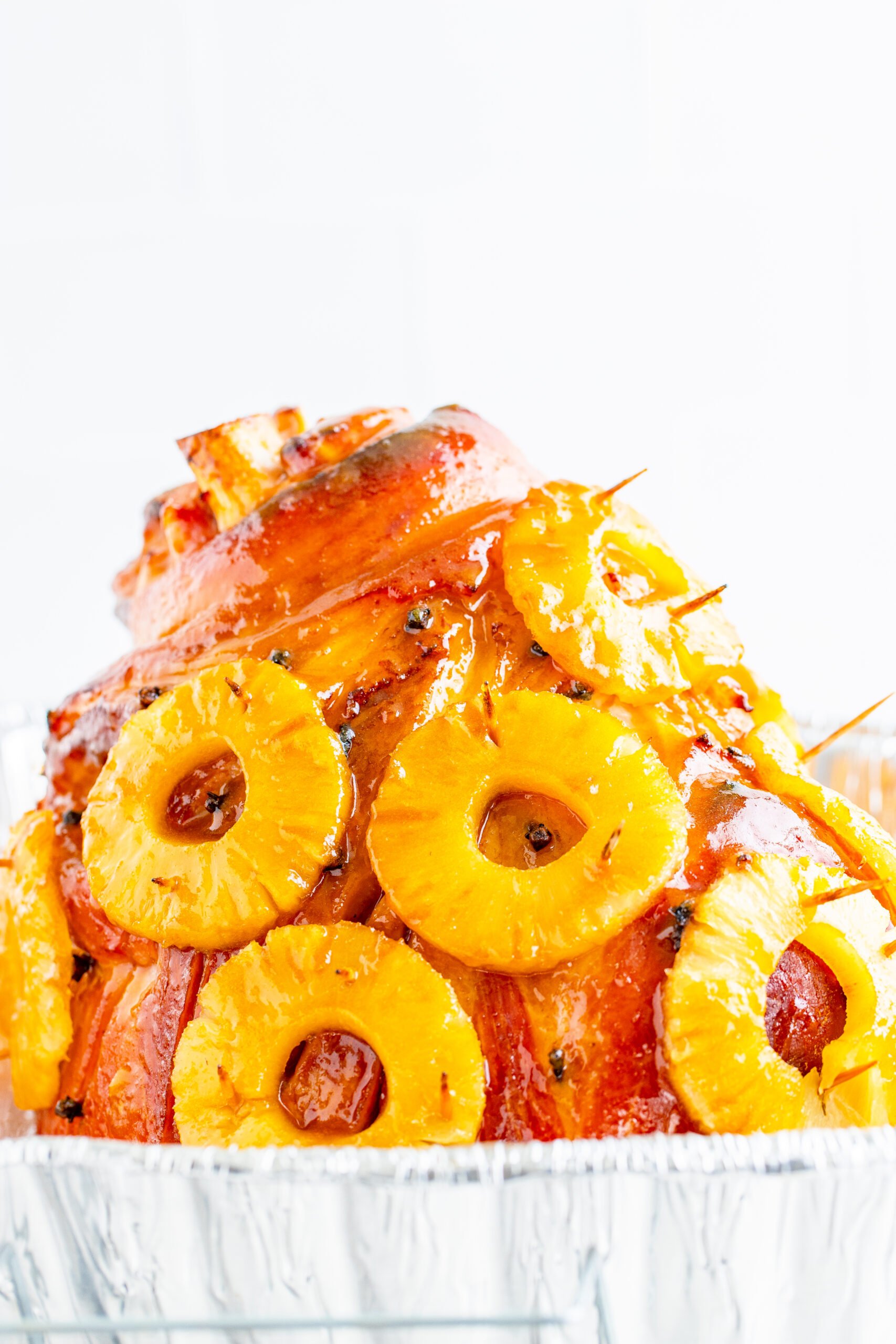 Pineapple Baked Ham covered in pineapple on a large white dish with oranges and pineapple slices lining the bottom.