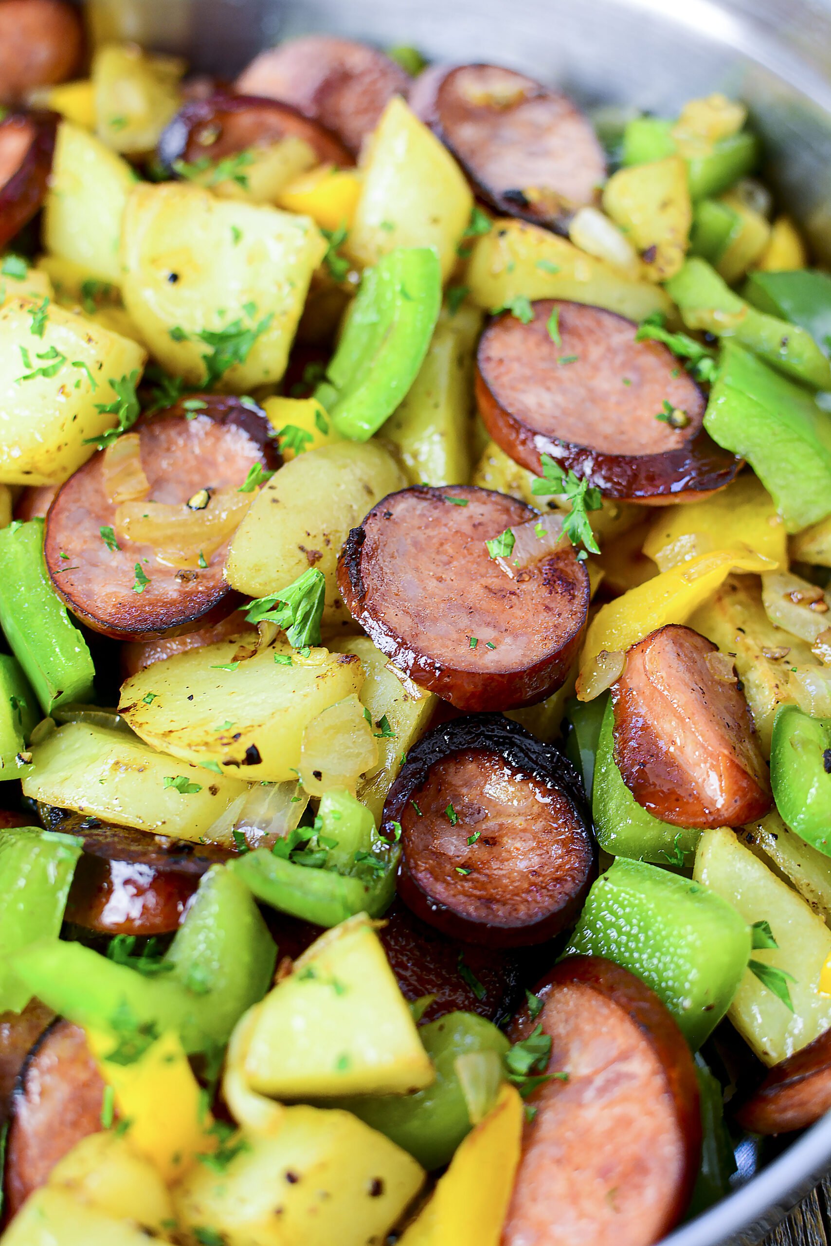 Close up view of sausage peppers and potatoes in a silvers skillet. 