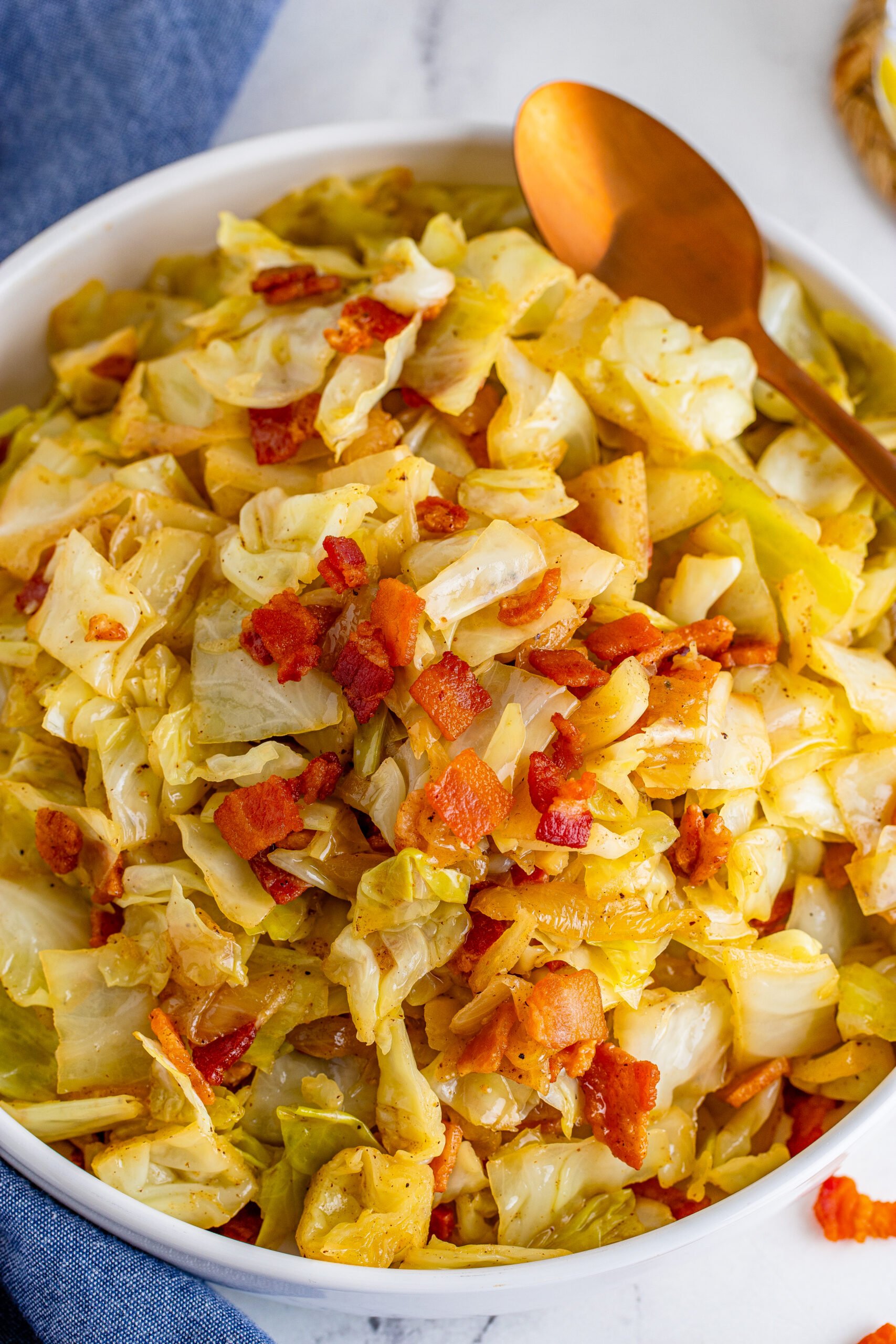 Bacon Fried Cabbage in a white bowl topped with bacon with a gold spoon on the side