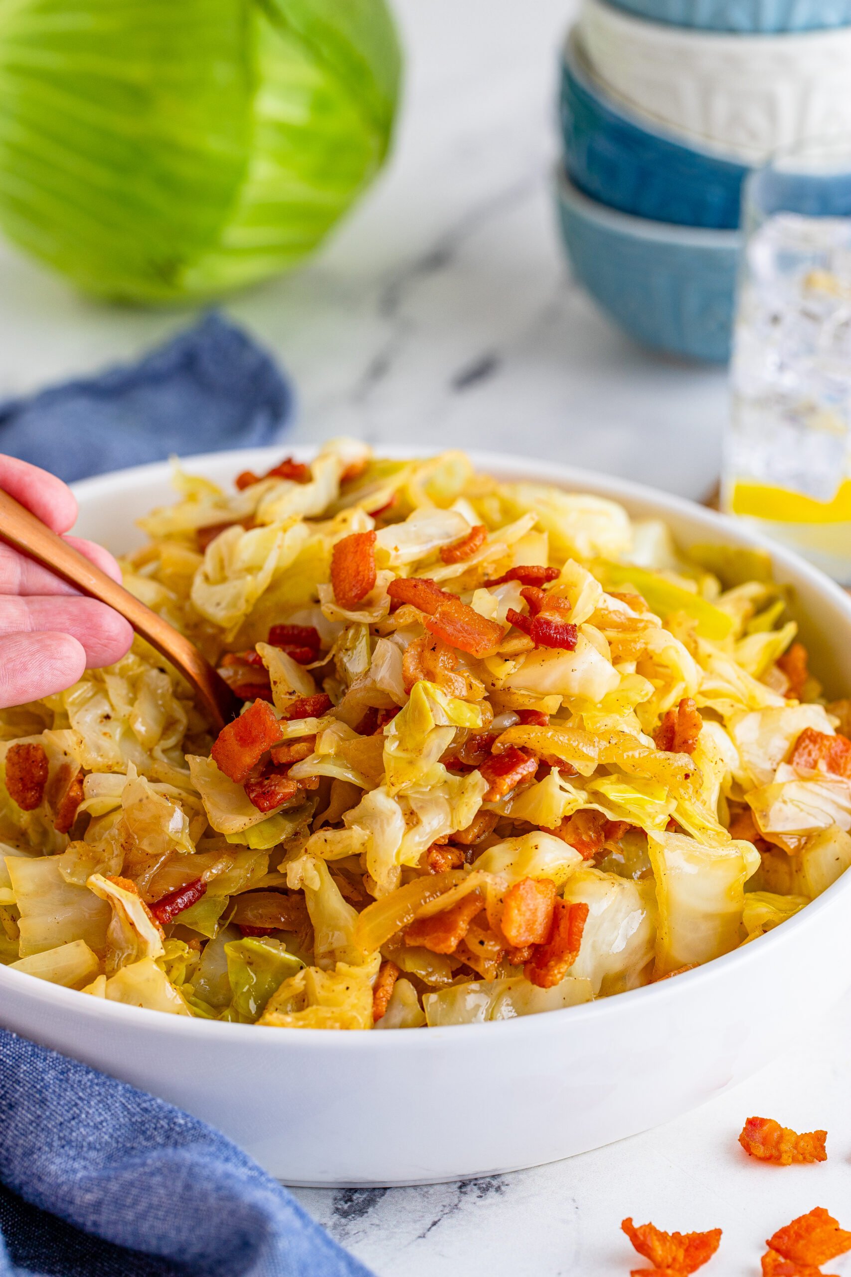 Fried Cabbage in a white bowl with a scoop being removed with a gold spoon. 