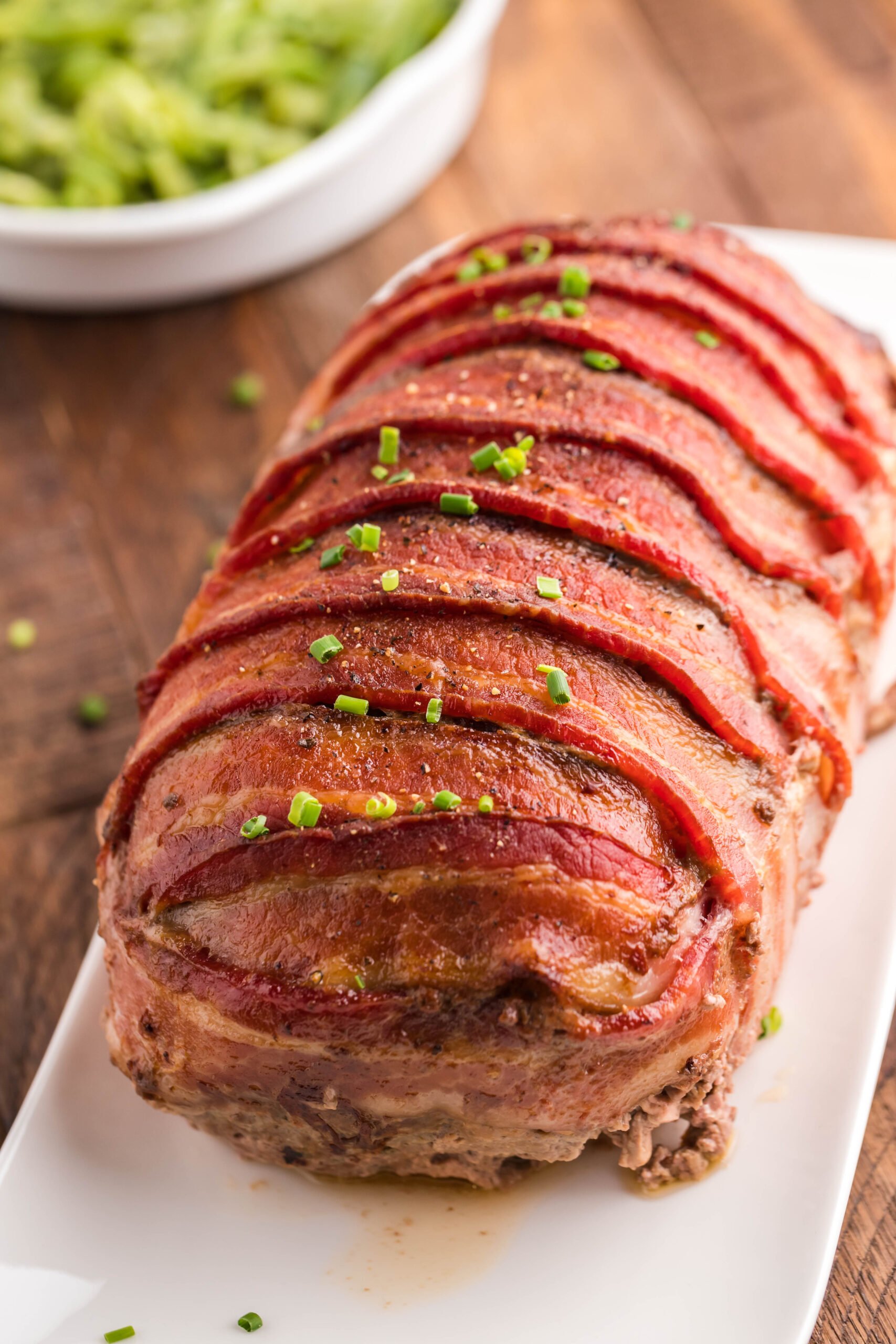 View of Bacon Wrapped Meatloaf on a white serving dish.