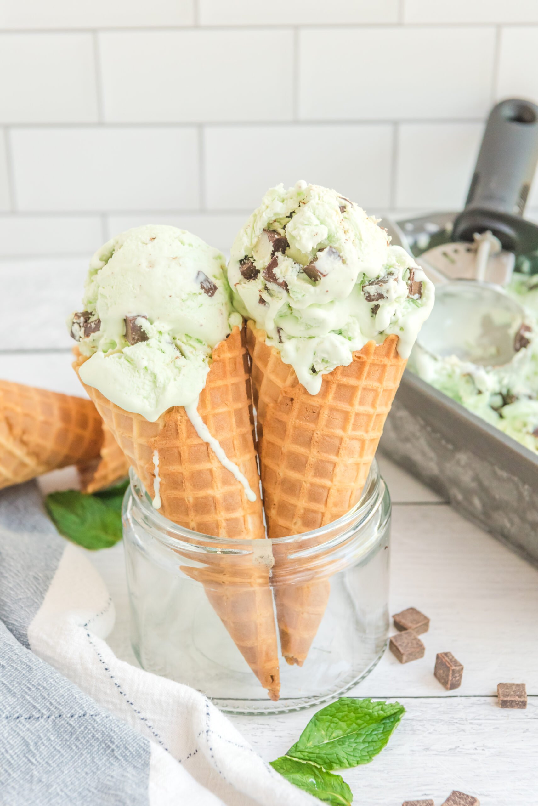 Front view of two scoops of Mint Chocolate Chip Ice Cream in two ice cream cones.