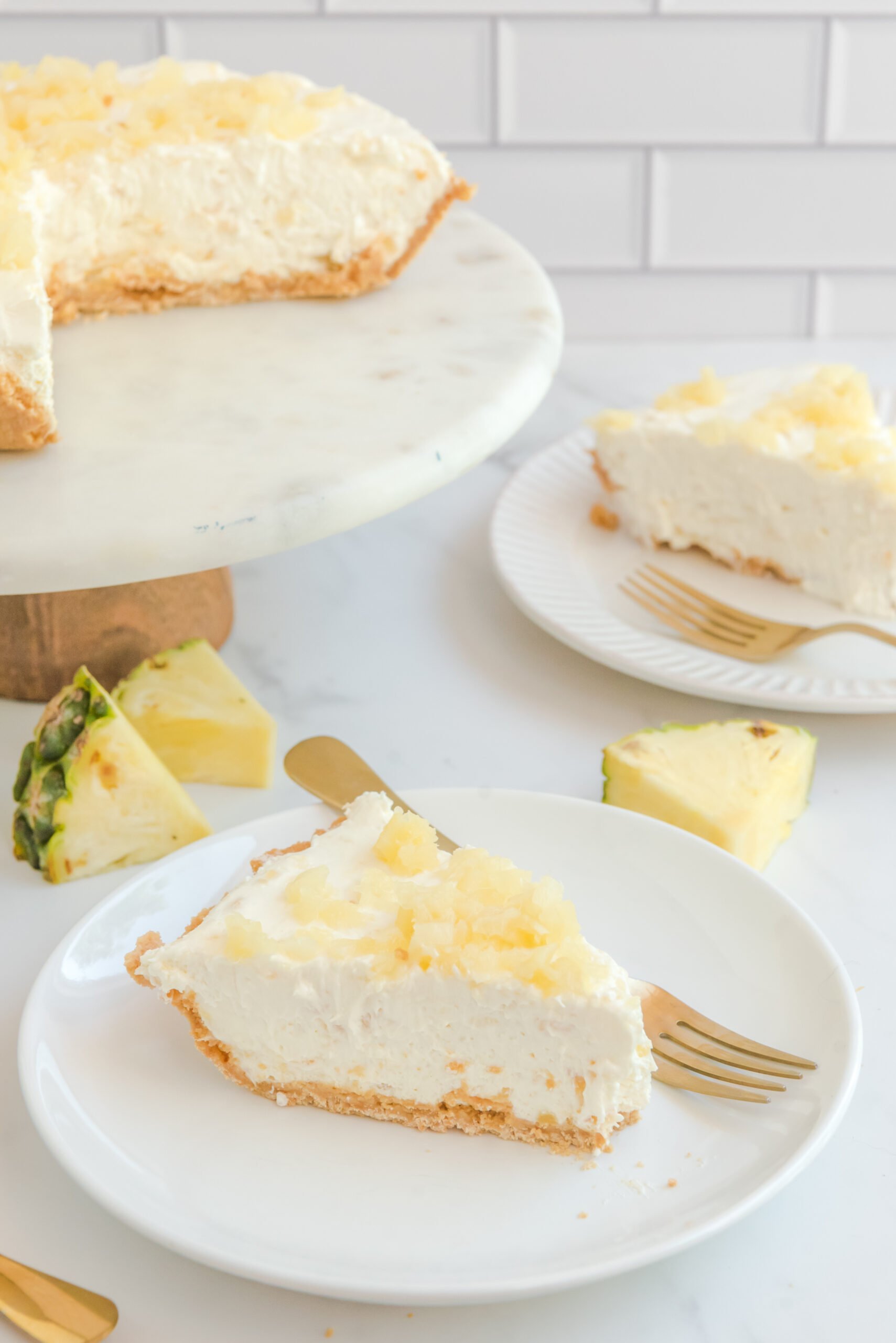 Front view of a slice of No Bake Pineapple Cheesecake on a white plate served with a gold fork.