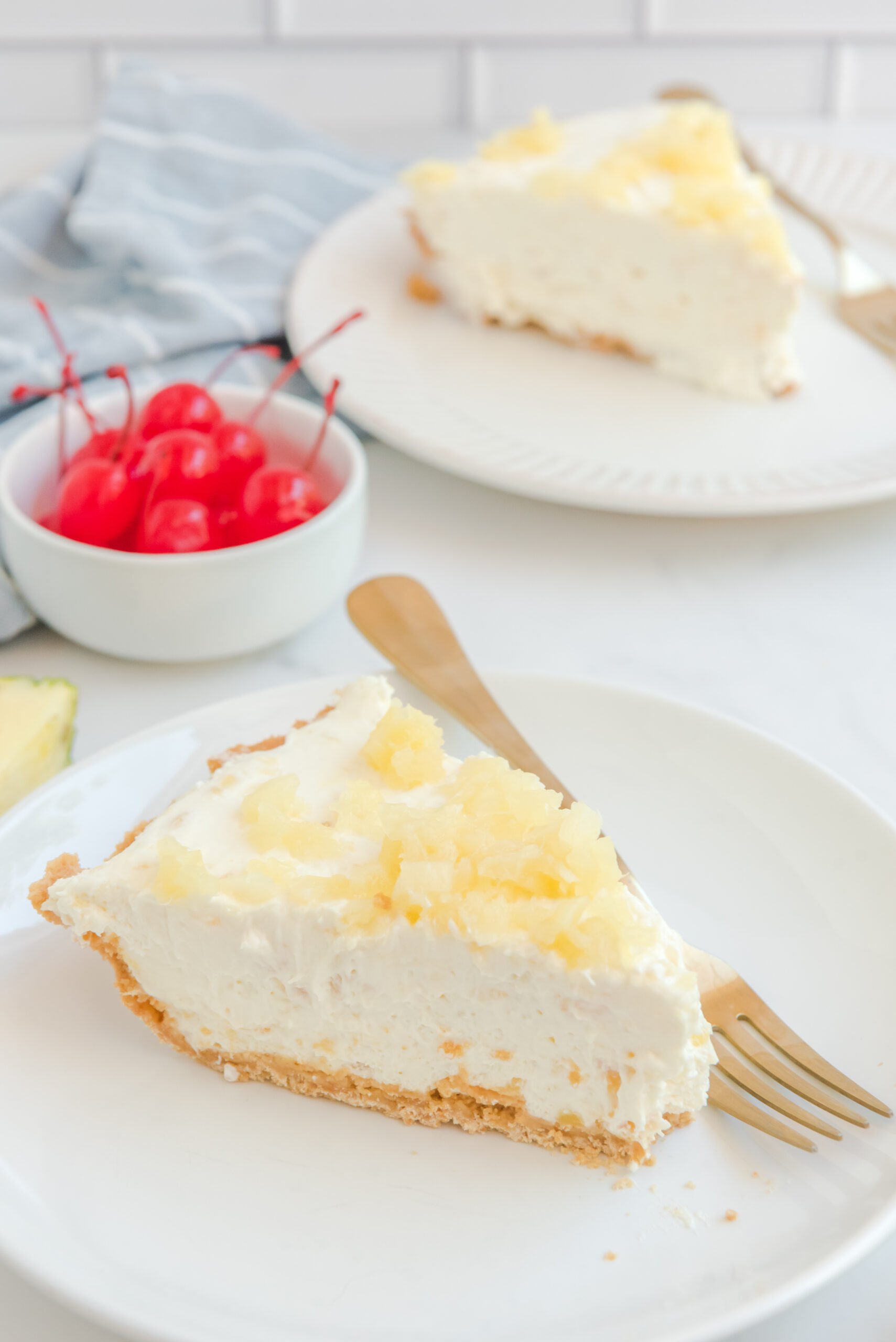 Side view of a slice of No Bake Pineapple Cheesecake served on a white plate with a gold fork.