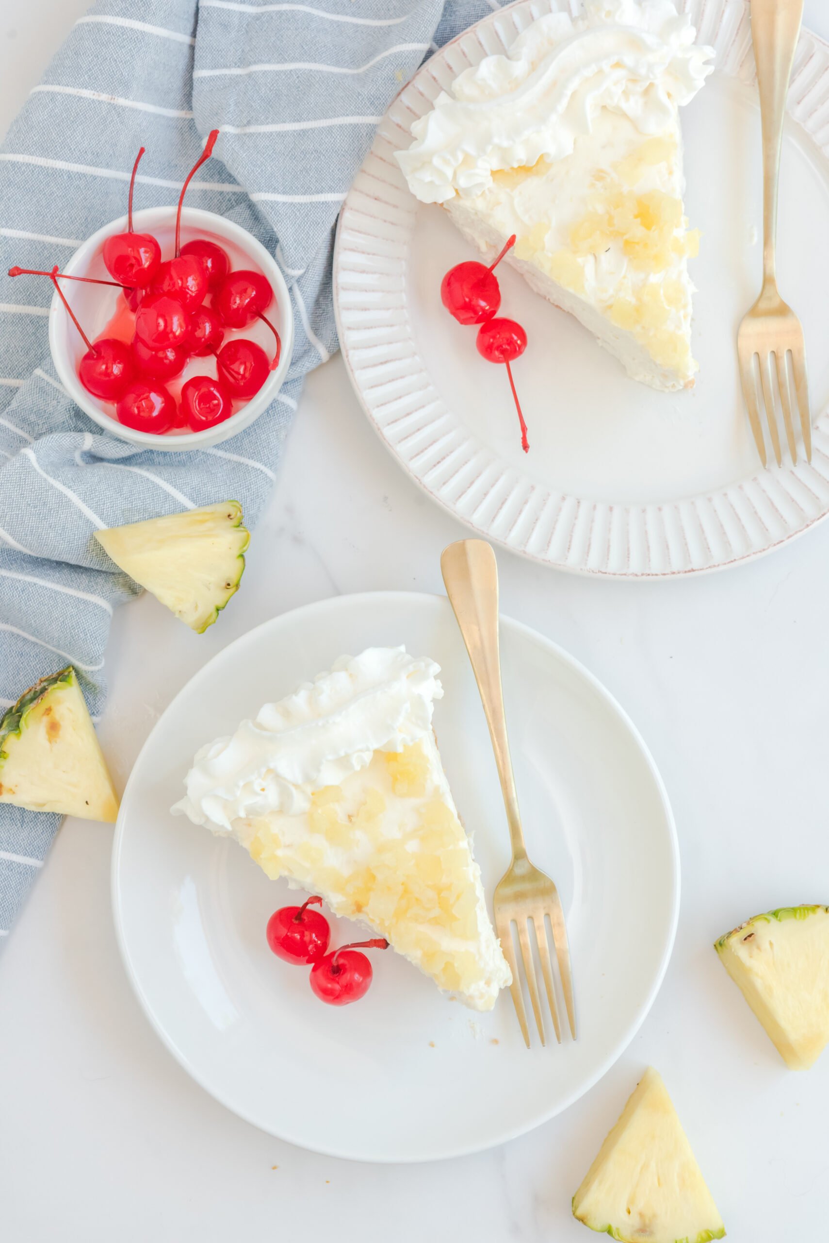 Overhead view of two slices of No Bake Pineapple Cheesecake served on white plates with gold forks.