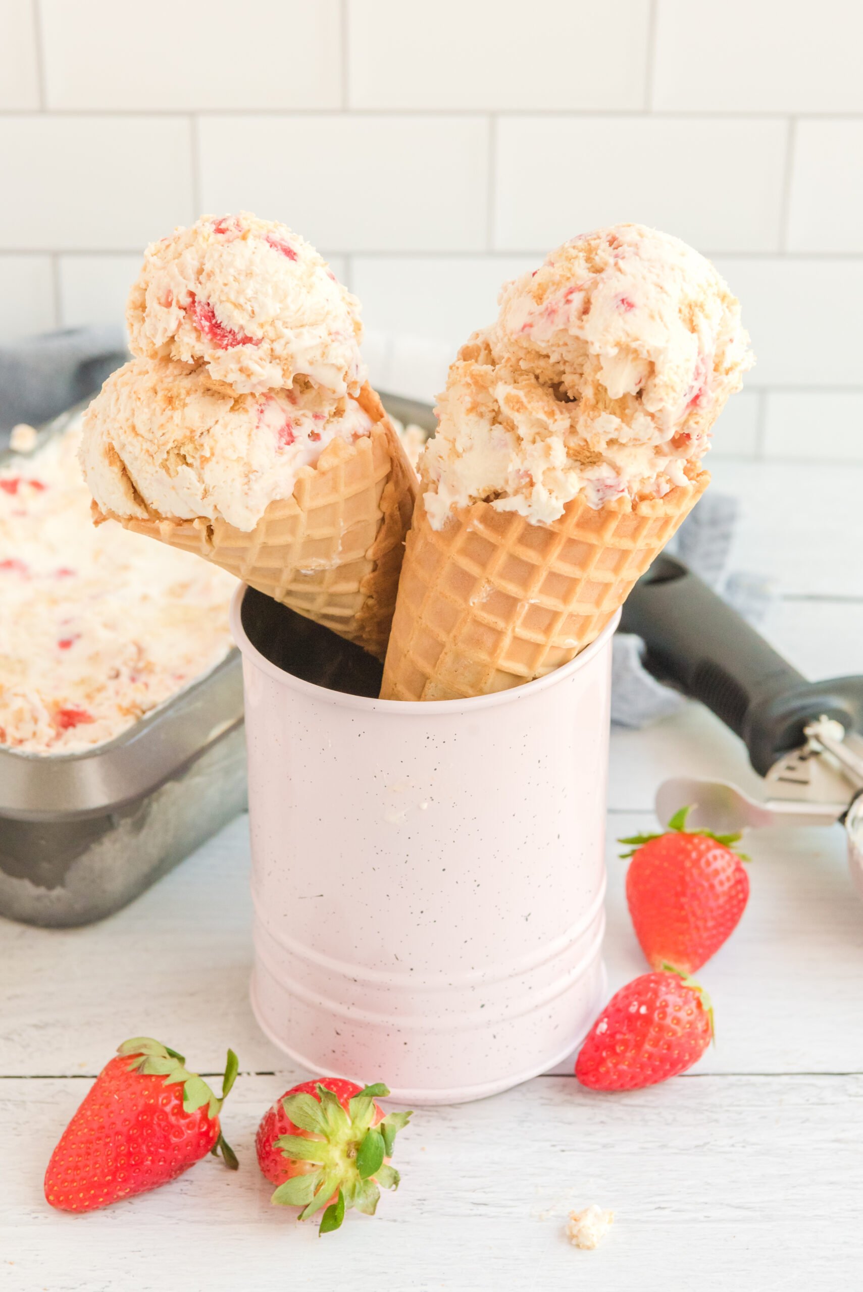 Front view of two waffle cones with a scoop of Strawberry Cheesecake Ice Cream in each cone.