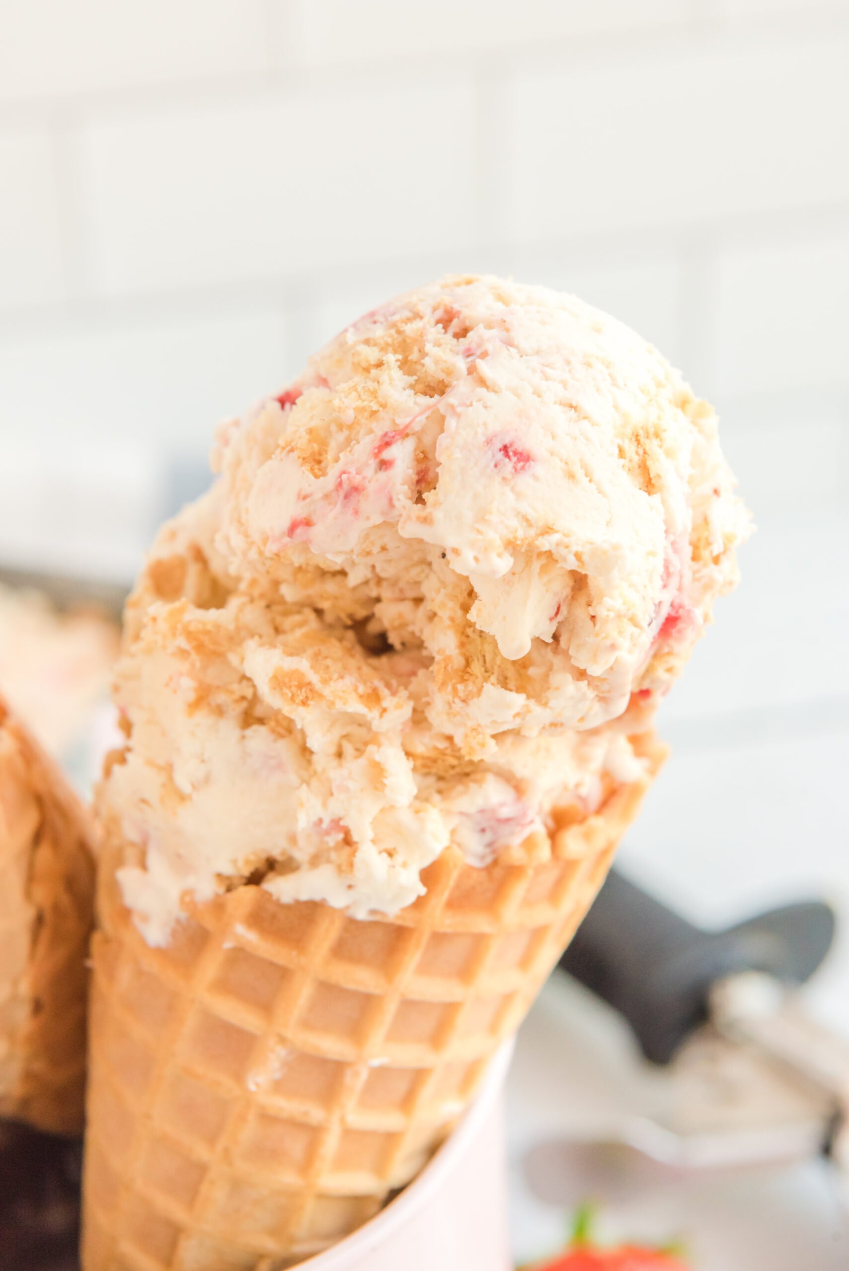 Close up view of a waffle cone with a scoop of Strawberry Cheesecake Ice Cream.