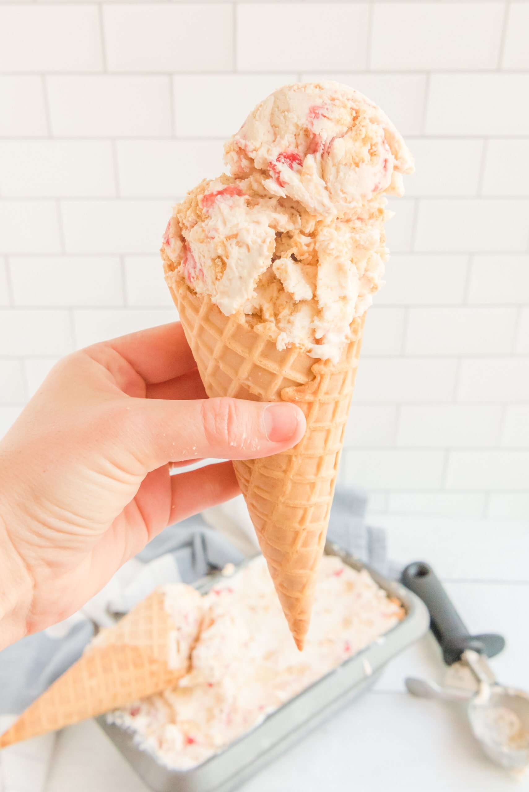 Front view of a waffle cone with a scoop of Strawberry Cheesecake Ice Cream.