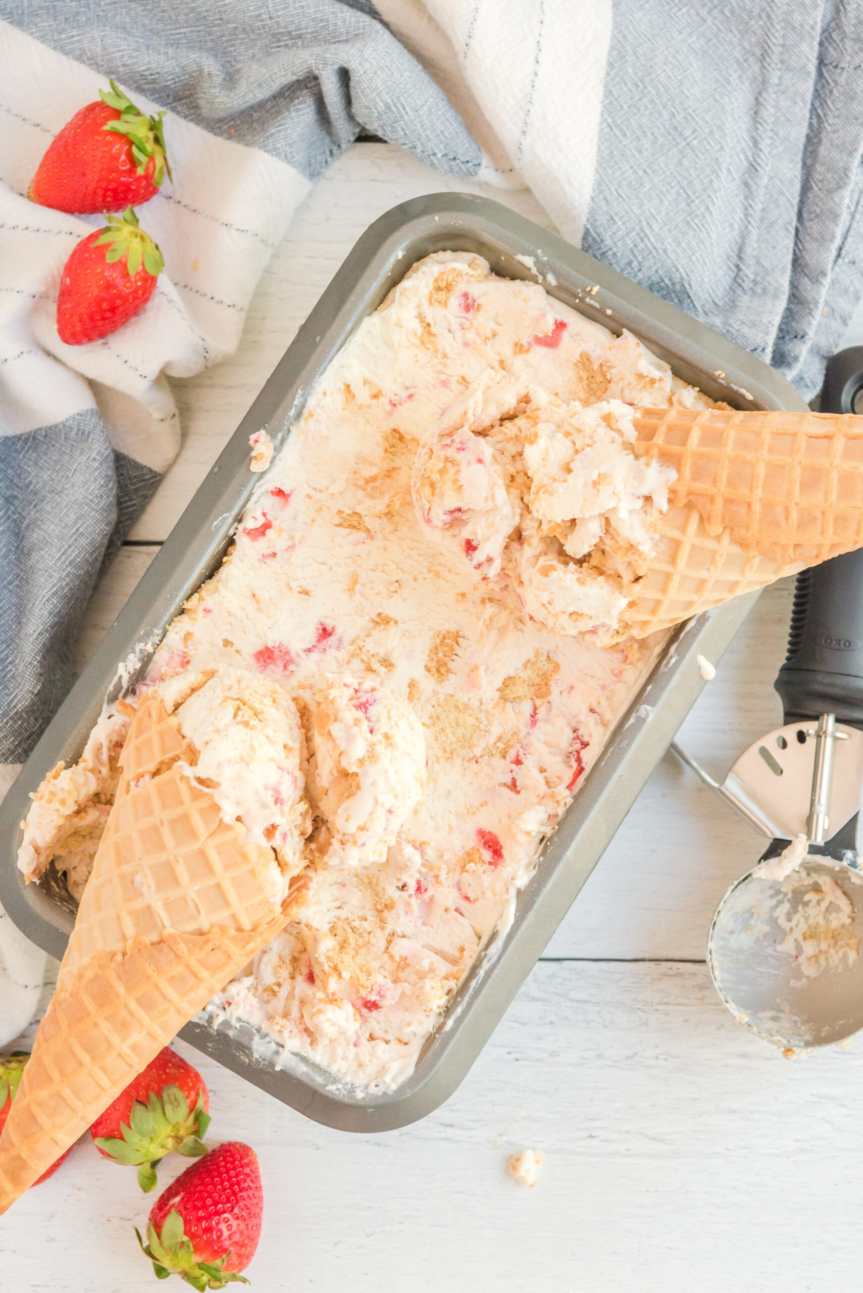 Overhead view of a pan full of Strawberry Cheesecake Ice Cream with two waffle cones laying on top.