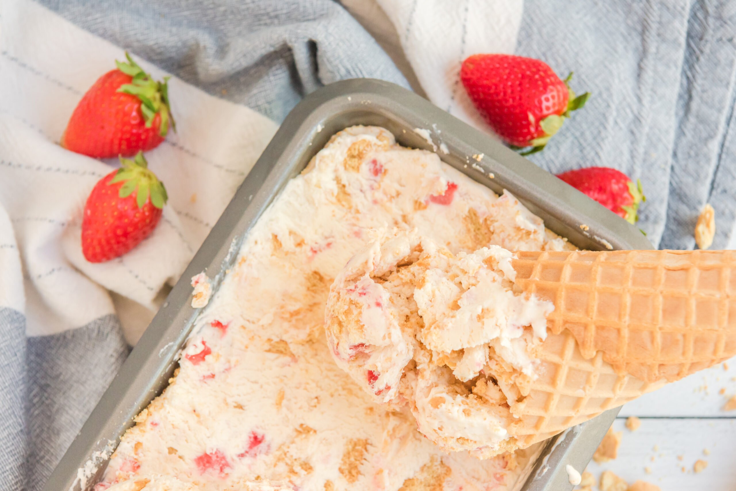 Strawberry Cheesecake Ice Cream with a cone dipping in it.