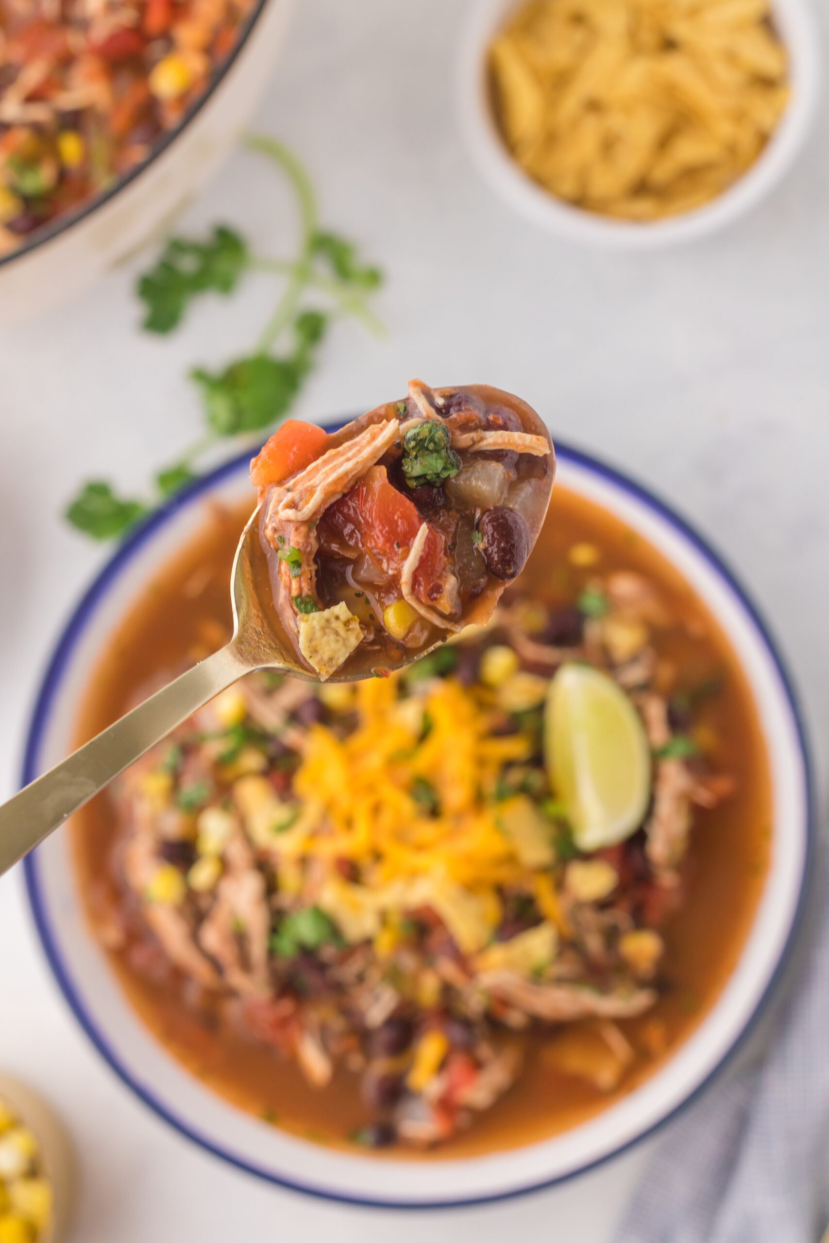 Overhead view of Chicken Taco Soup in a bowl with a spoonful of soup in a gold spoon.