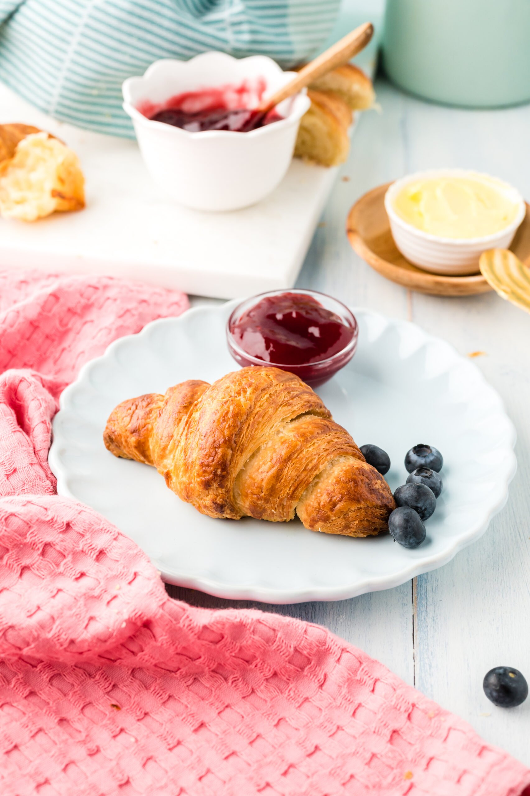 Front view of Homemade Croissants served on a white dish with jam and fresh blueberries.
