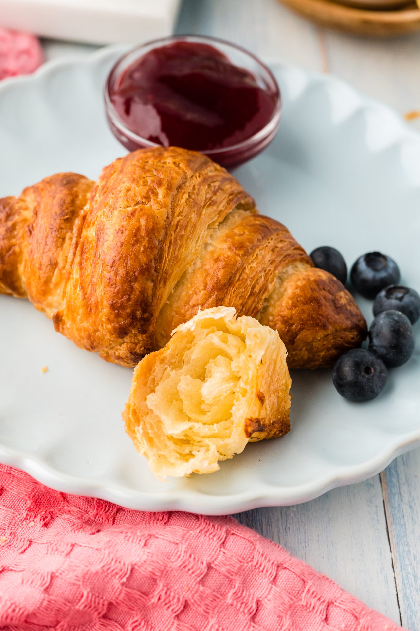 Front view of Homemade Croissants served on a white dish with jam and fresh blueberries.