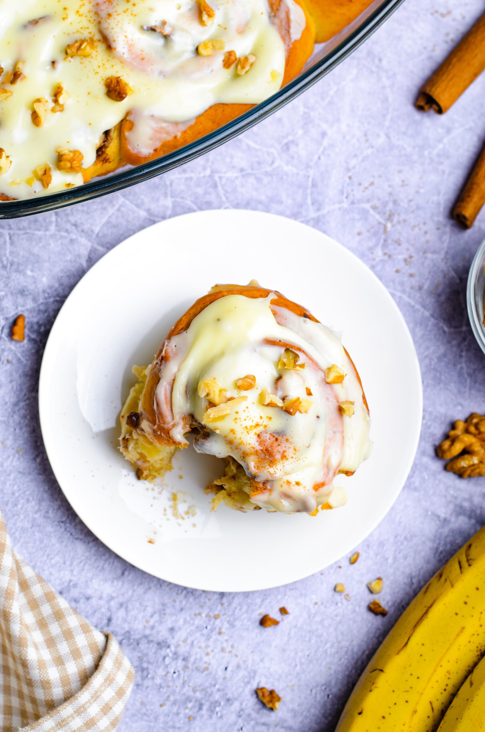 Overhead view of a Banana Nut Cinnamon Roll on a plate with a bite removed.