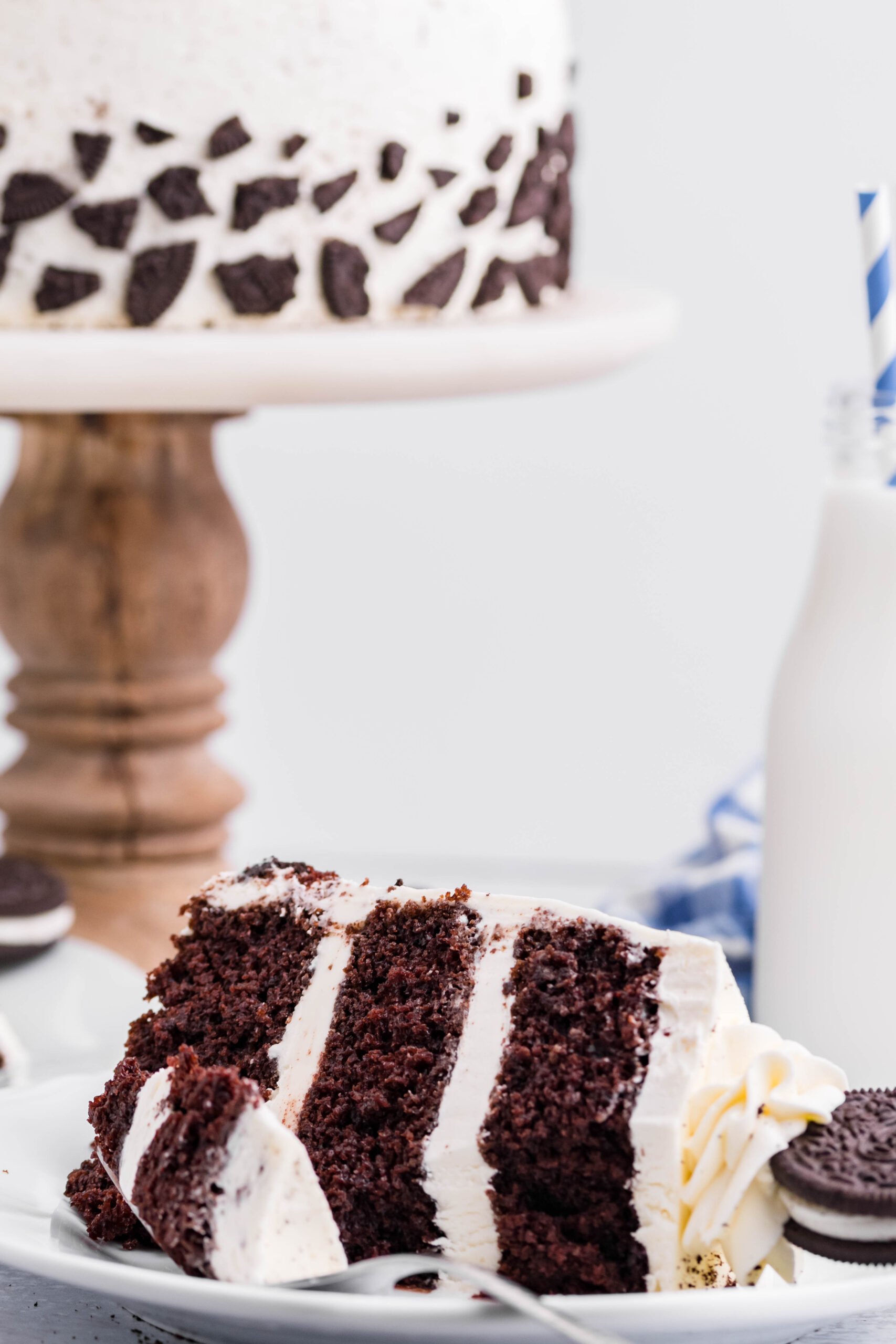 Front view of a slice of Double Stuffed Oreo Cake served on a white plate with a bite removed from a silver fork.