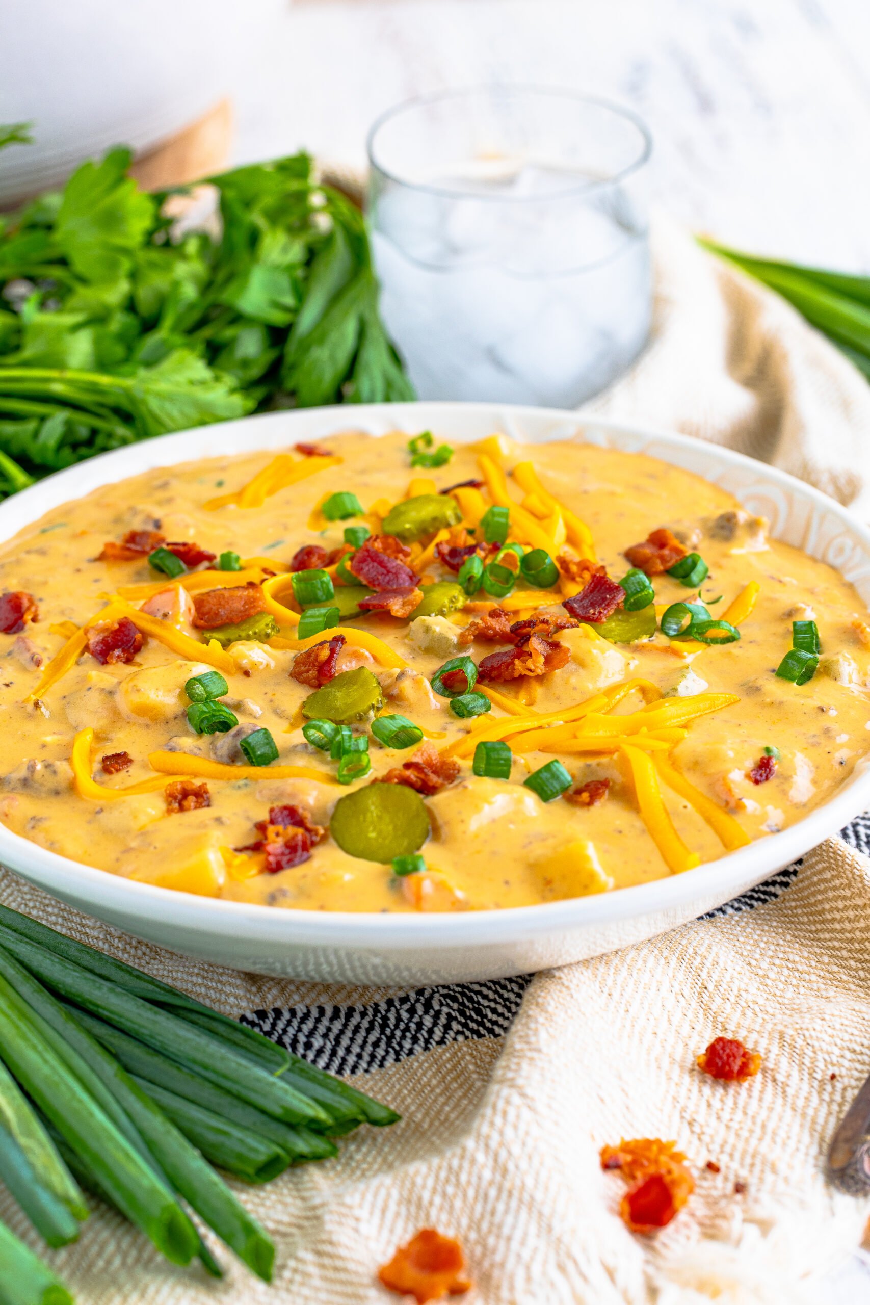 Cheeseburger bacon soup in a white bowl topped with bacon, cheese, and green onion. 