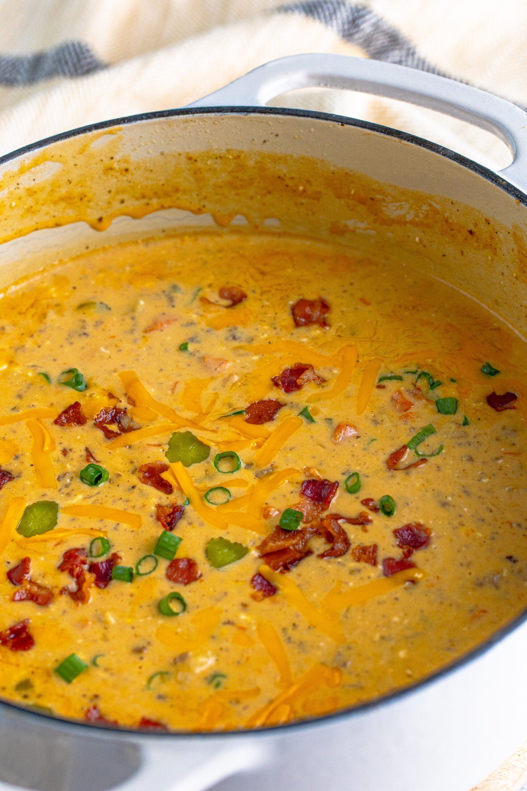 white dutch oven pot filled with Bacon Cheeseburger Soup topped with sprinkled bacon pieces