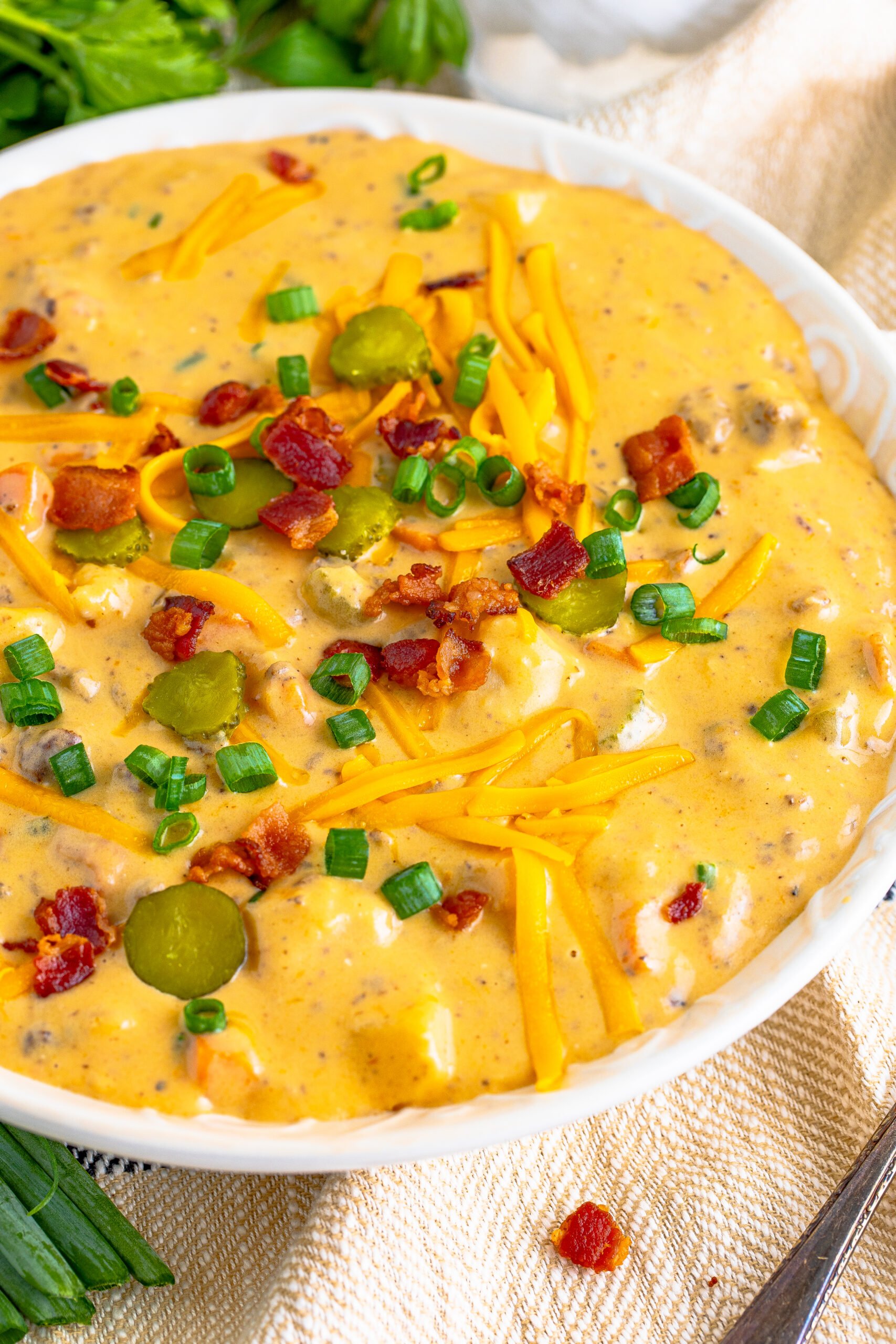 Cheeseburger bacon soup in a white bowl topped with bacon, cheese, and green onion. 