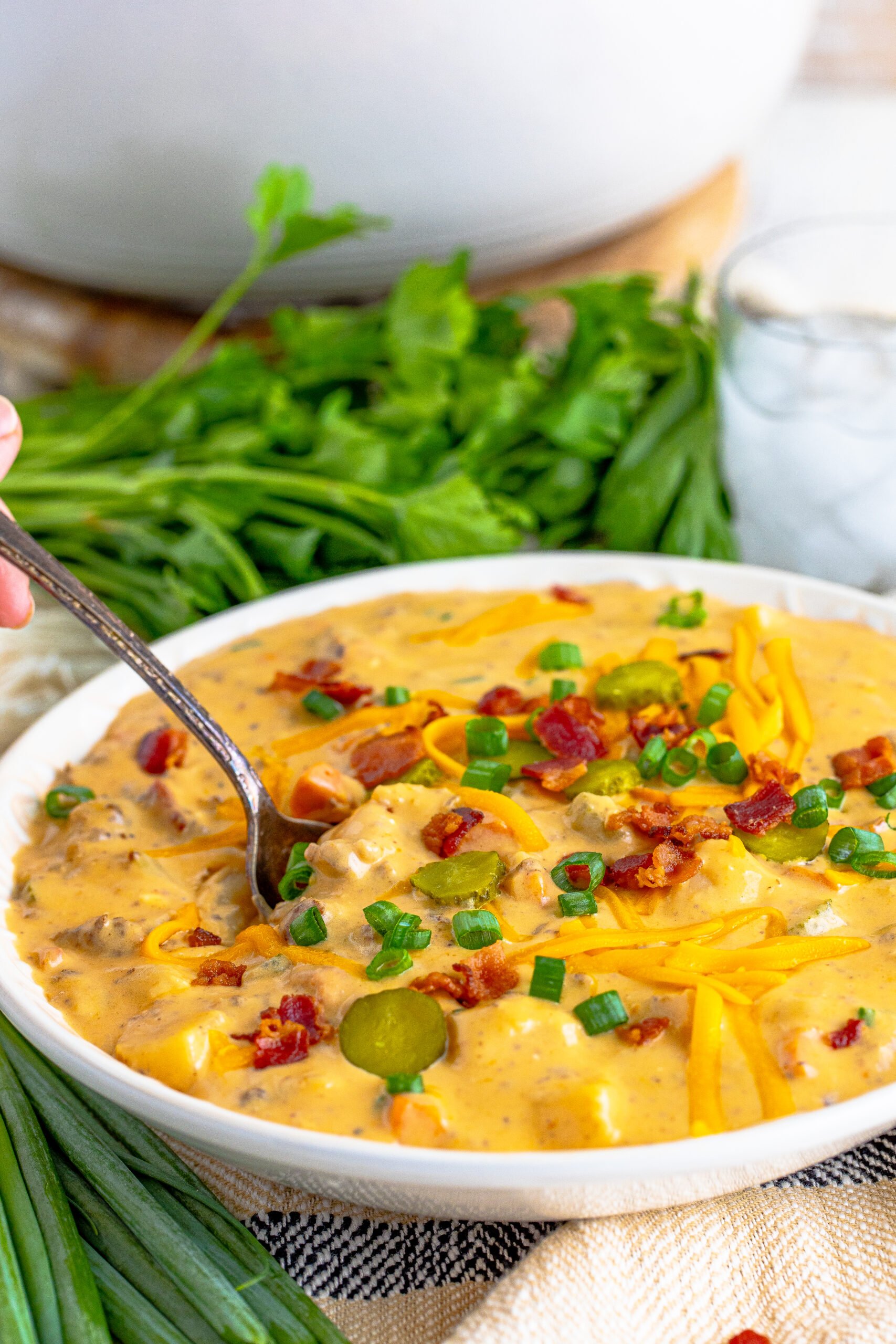 Cheeseburger bacon soup in a white bowl with a silver spoon removing a bite. 