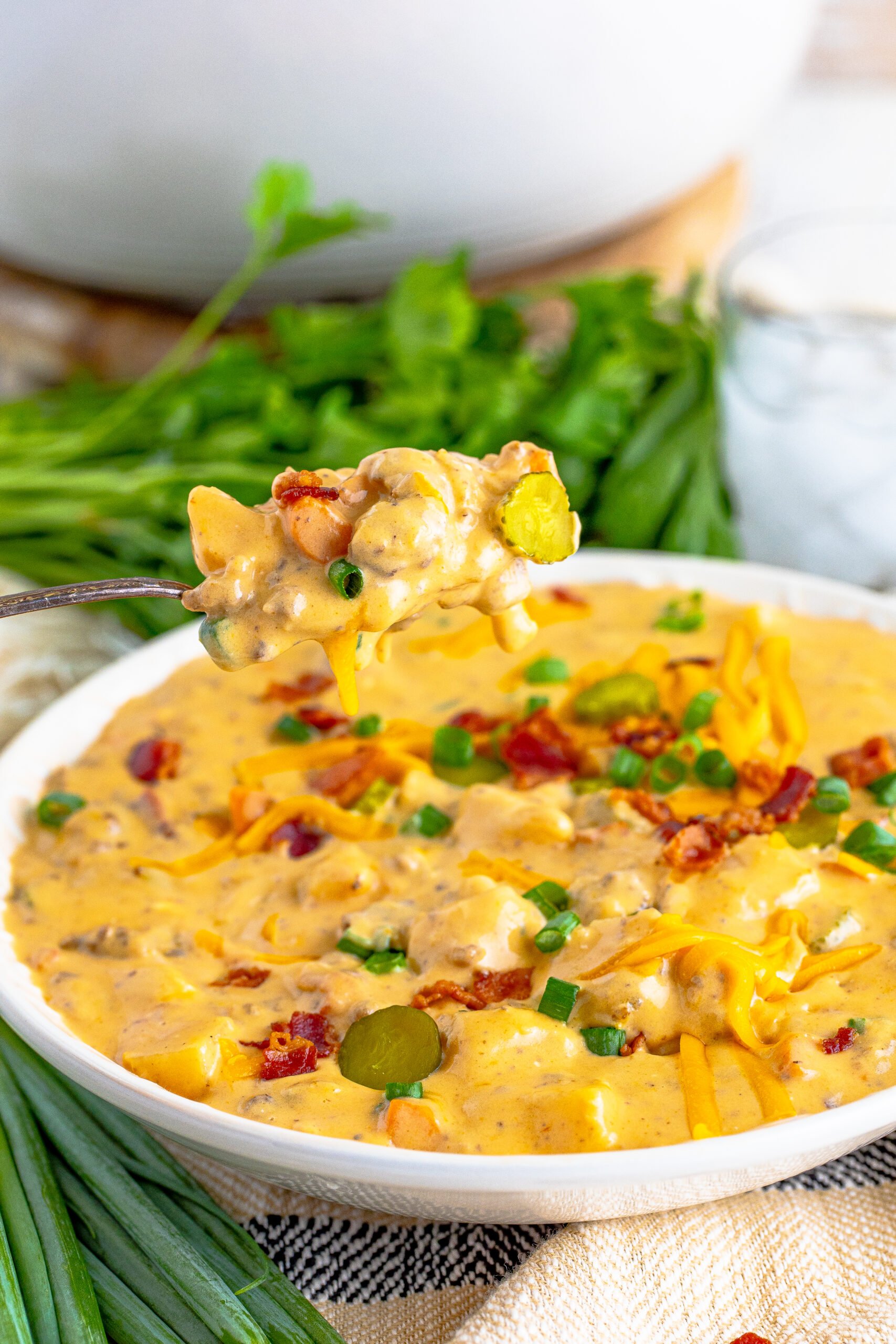 Cheeseburger bacon soup in a white bowl with a silver spoon removing a bite. 