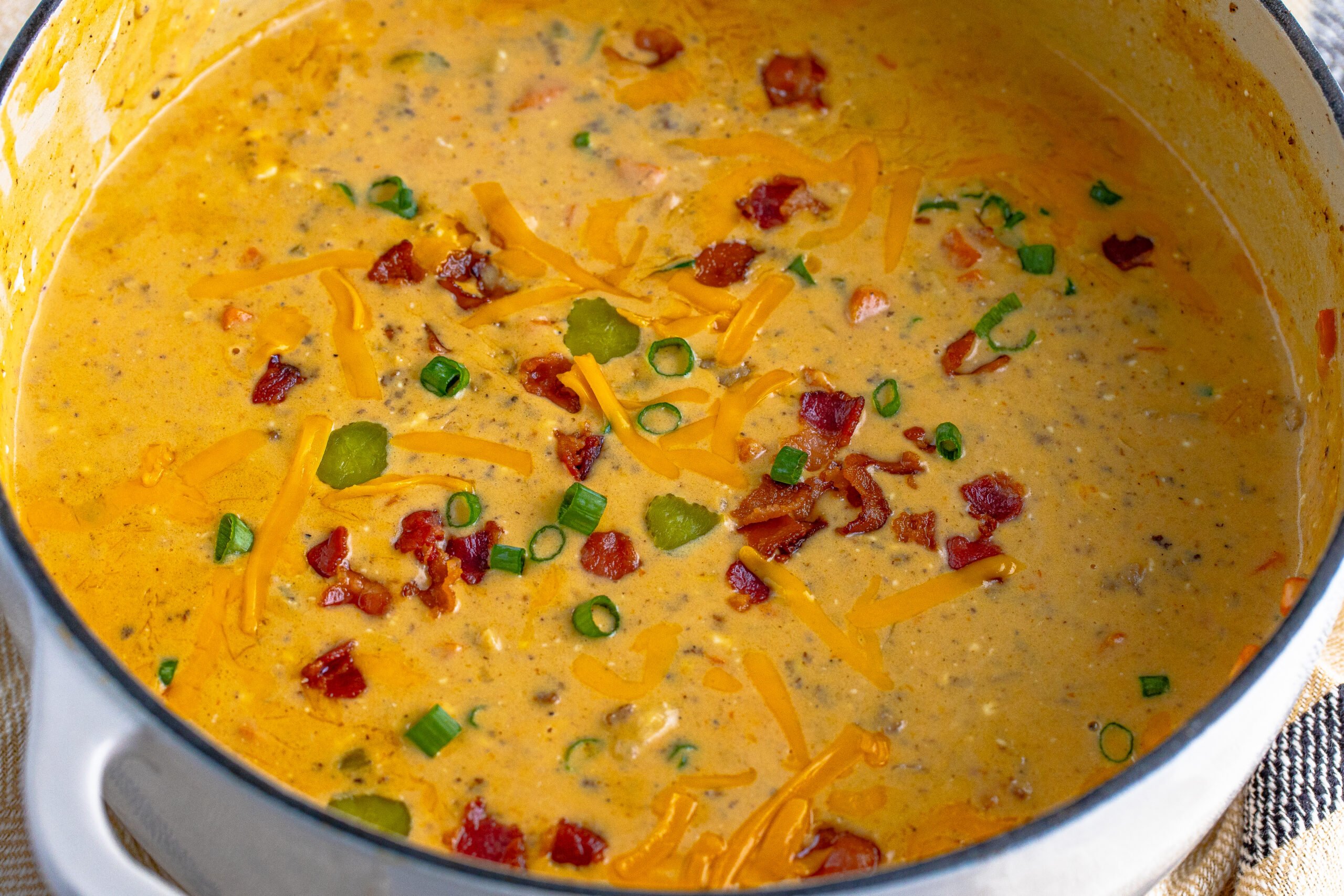 white dutch oven pot filled with Bacon Cheeseburger Soup topped with sprinkled bacon pieces