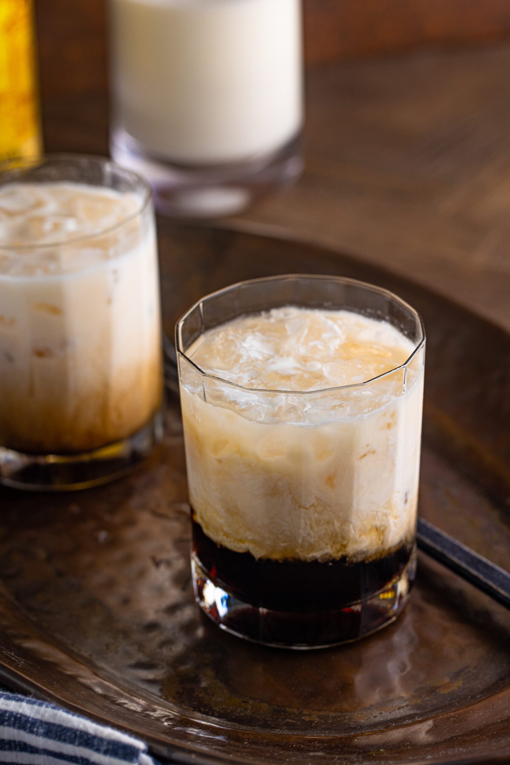 White Russian in a clear glass sitting on a dark metal serving tray. 