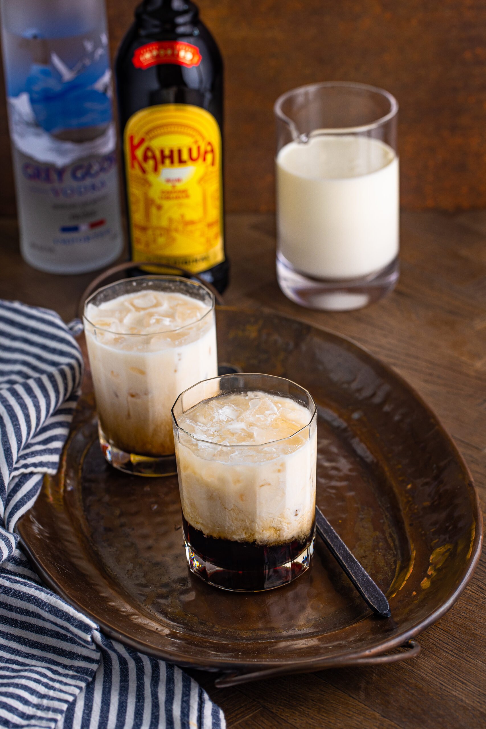 White Russian in a clear glass sitting on a dark metal serving tray. 