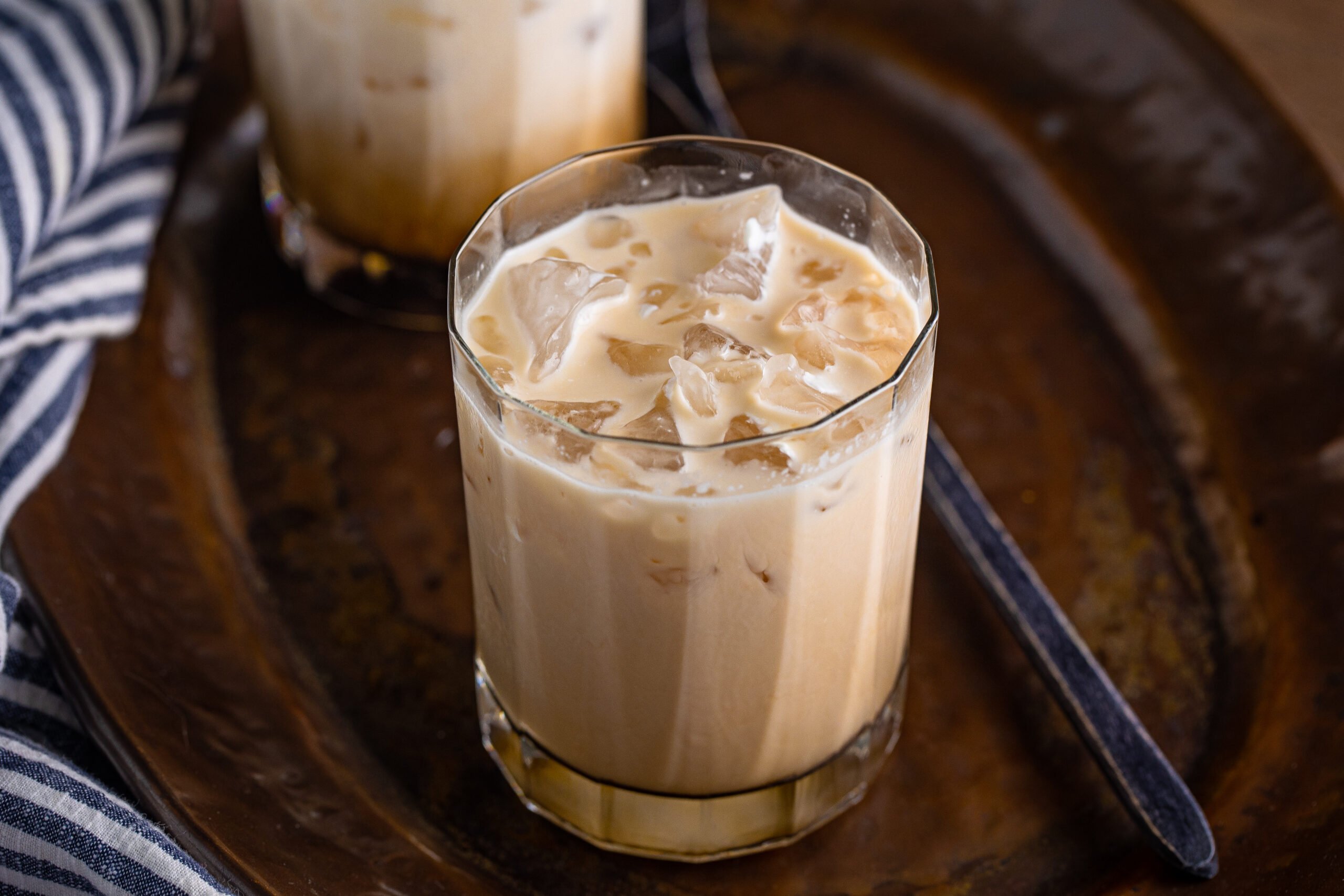 White Russian mixed in a clear glass sitting on a dark metal serving tray. 