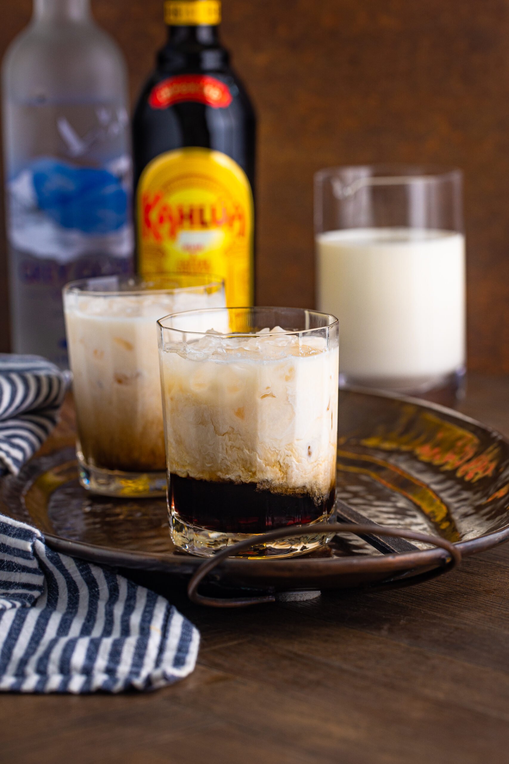 White Russian in a clear glass sitting on a dark metal serving tray. 