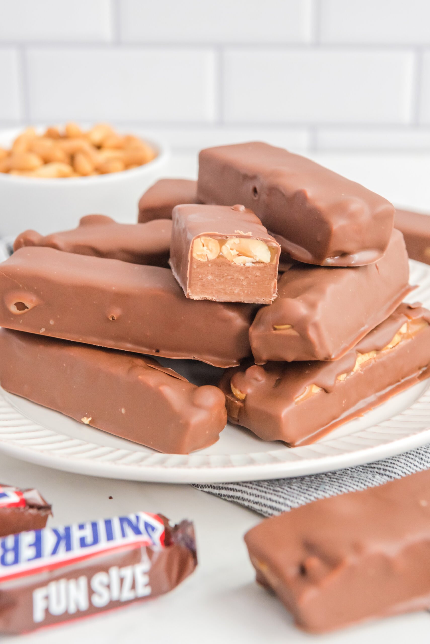 Front view of Homemade Snickers Bars stacked on a white plate with on bar cut in half.