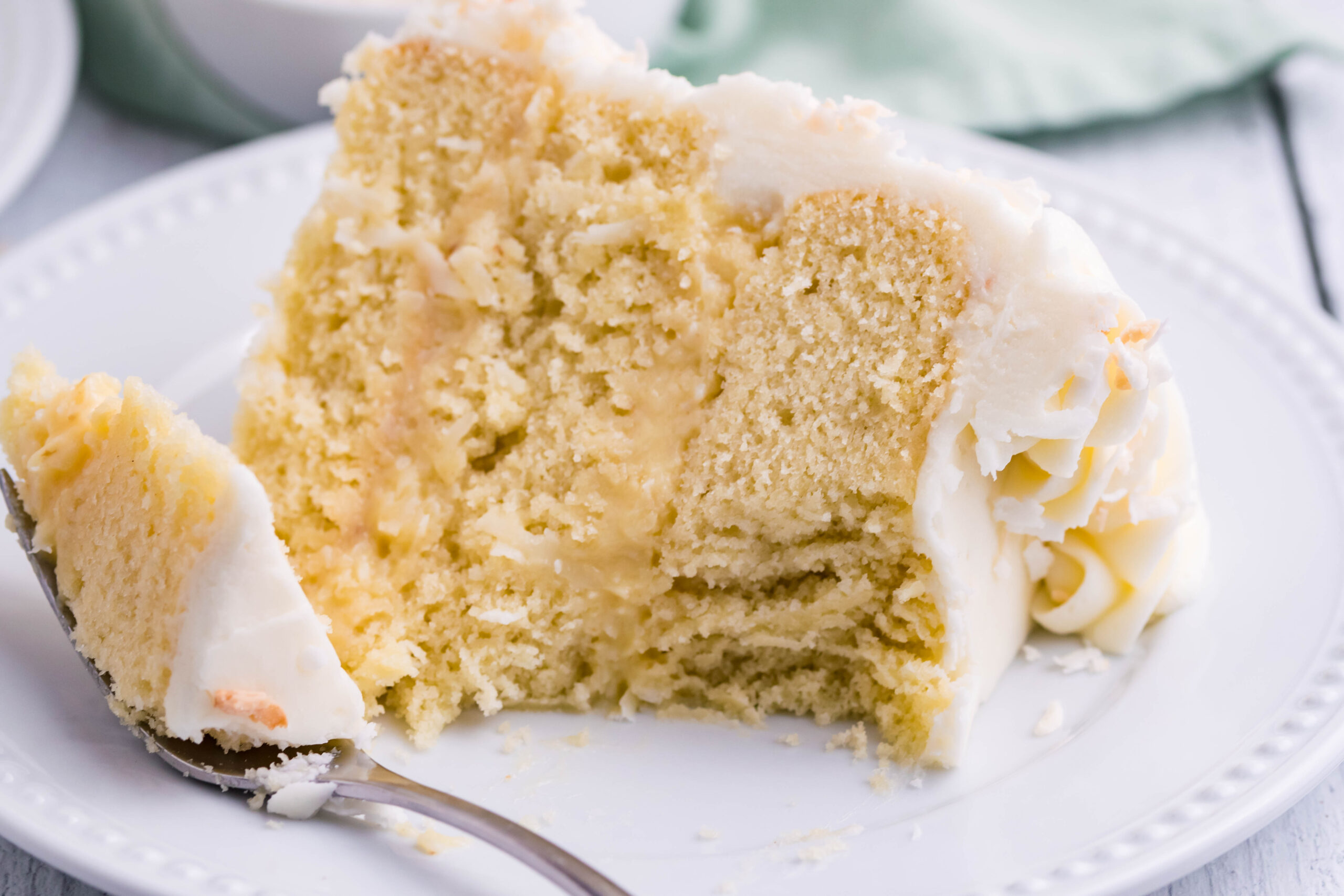 Front view of a slice of Coconut Custard Cake on a white plate with a bite removed by a silver fork.