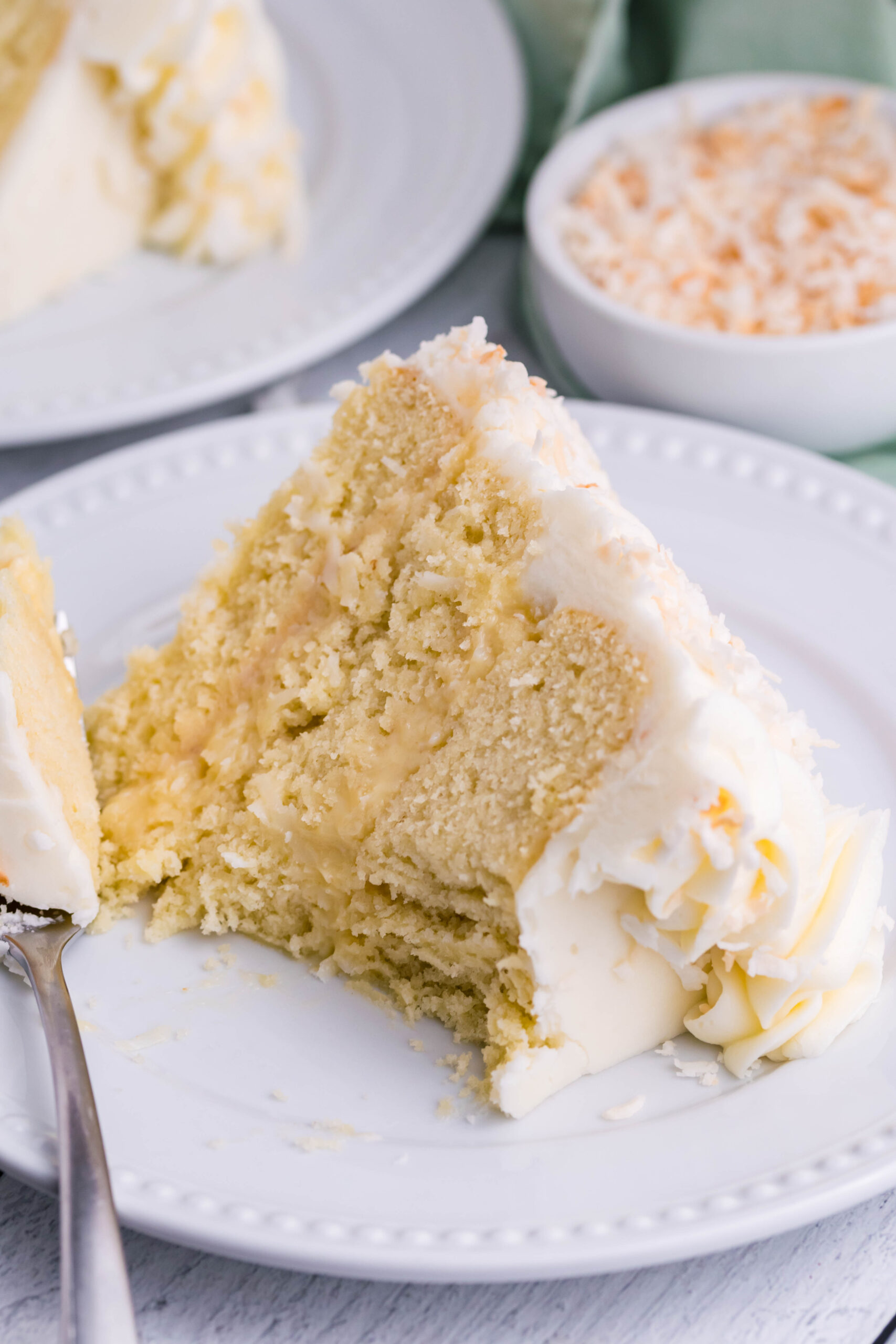 Front view of a slice of Coconut Custard Cake on a white plate with a bite removed by a silver fork.
