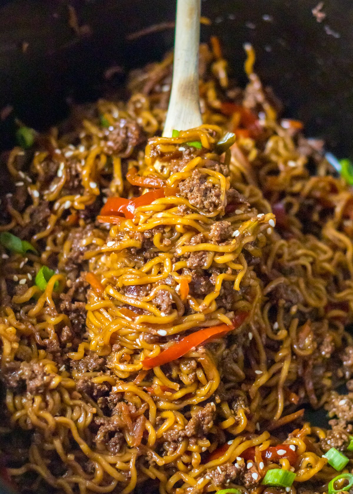 Close up view of Slow Cooker Beef Ramen in a crock pot with a wooden spoon removing a serving.