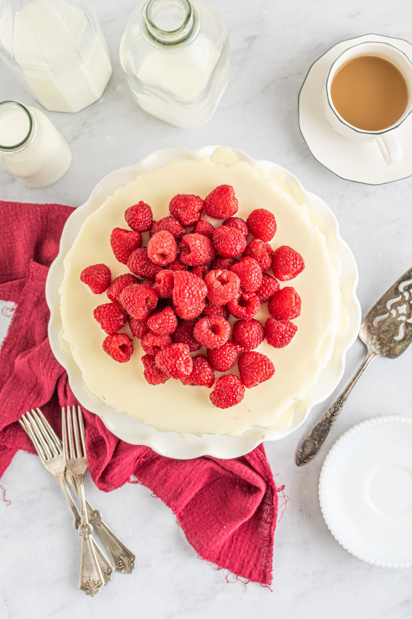 Overhead view of White Chocolate Cake with Raspberries on a white cake stand.