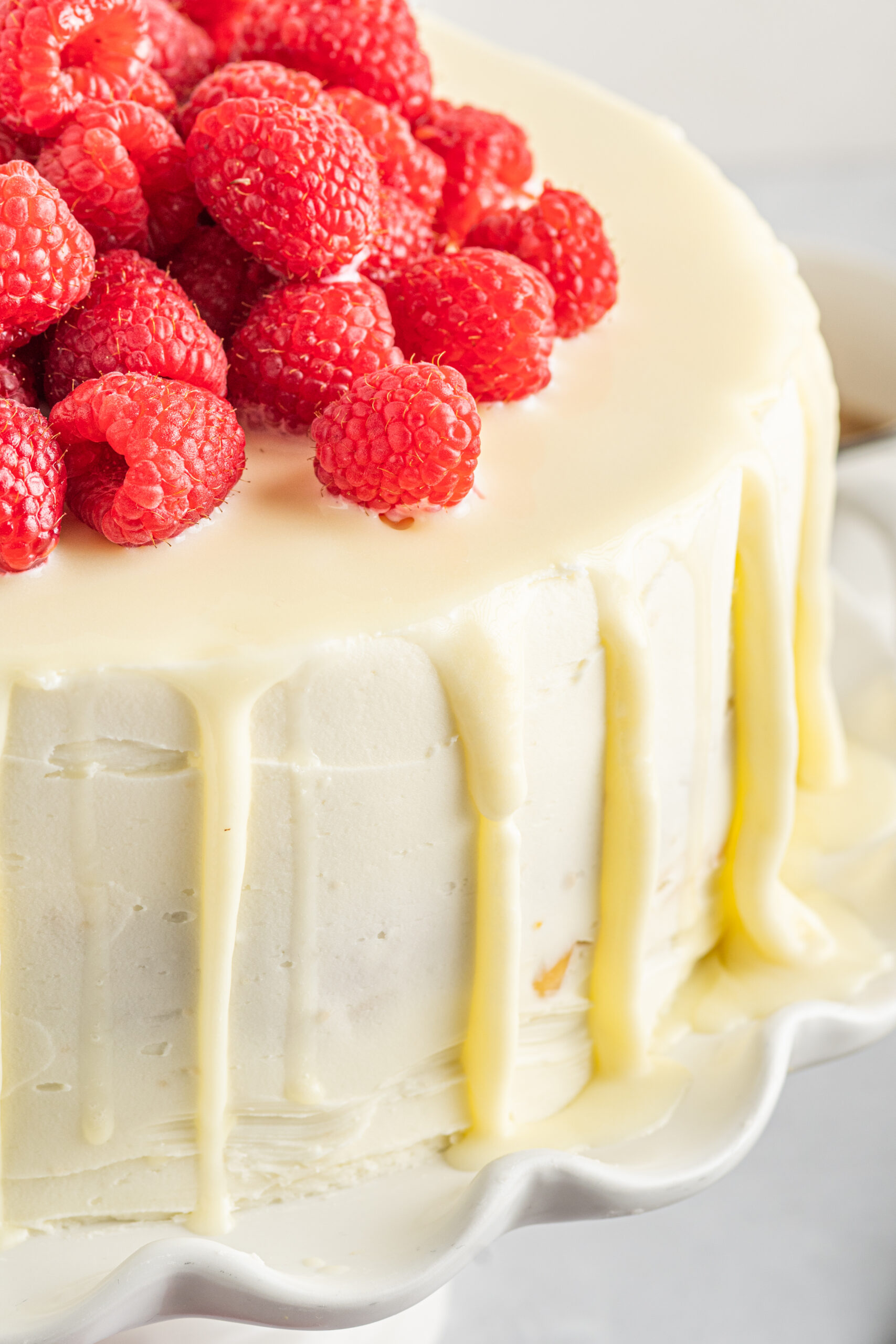 Up close view of White Chocolate Cake with Raspberries on a white cake stand.