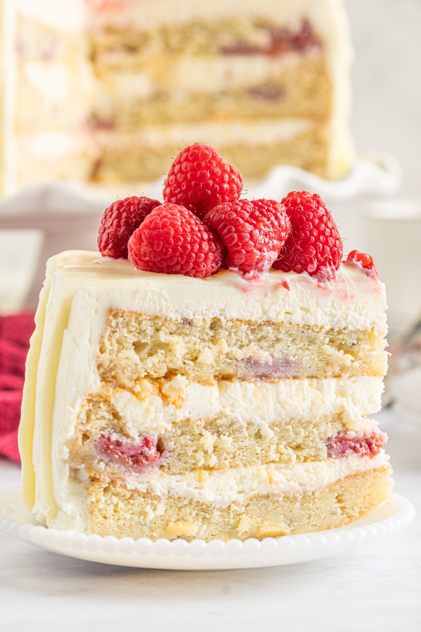 Side view of a slice of White Chocolate Cake with Raspberries on a white plate.