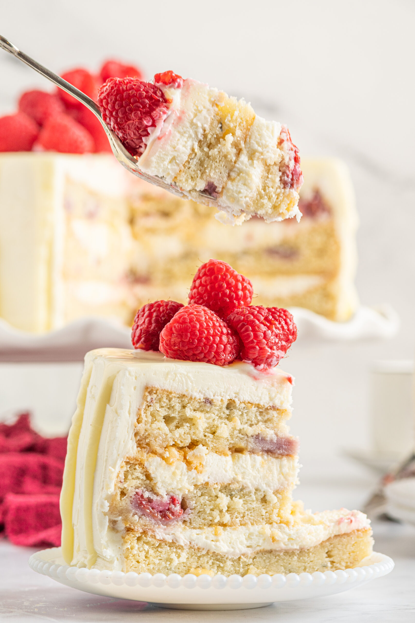 Side view of a bite of White Chocolate Cake with Raspberries on a silver fork.