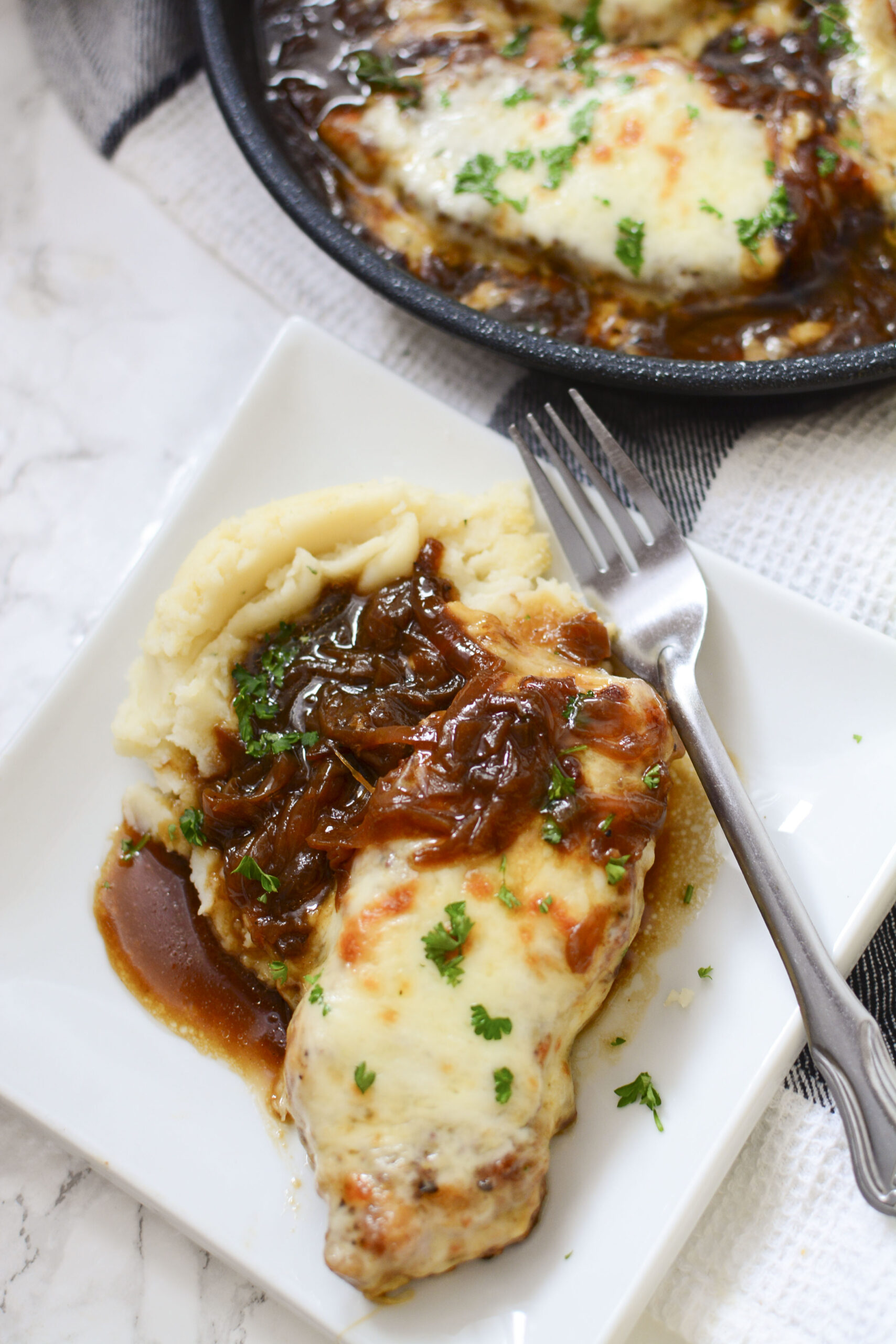 Overhead view of French Onion Pork Chops served with mashed potatoes and silver fork on a white plate.