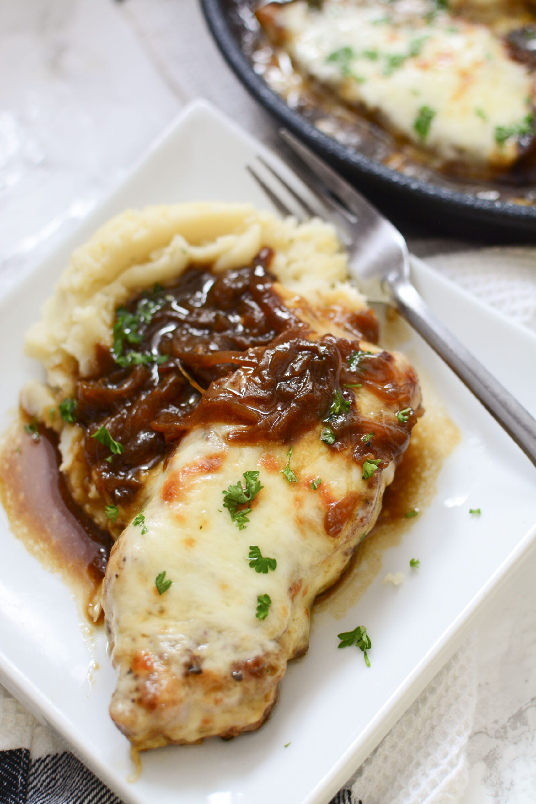 Close up view of French Onion Pork Chops served with mashed potatoes and silver fork on a white plate.