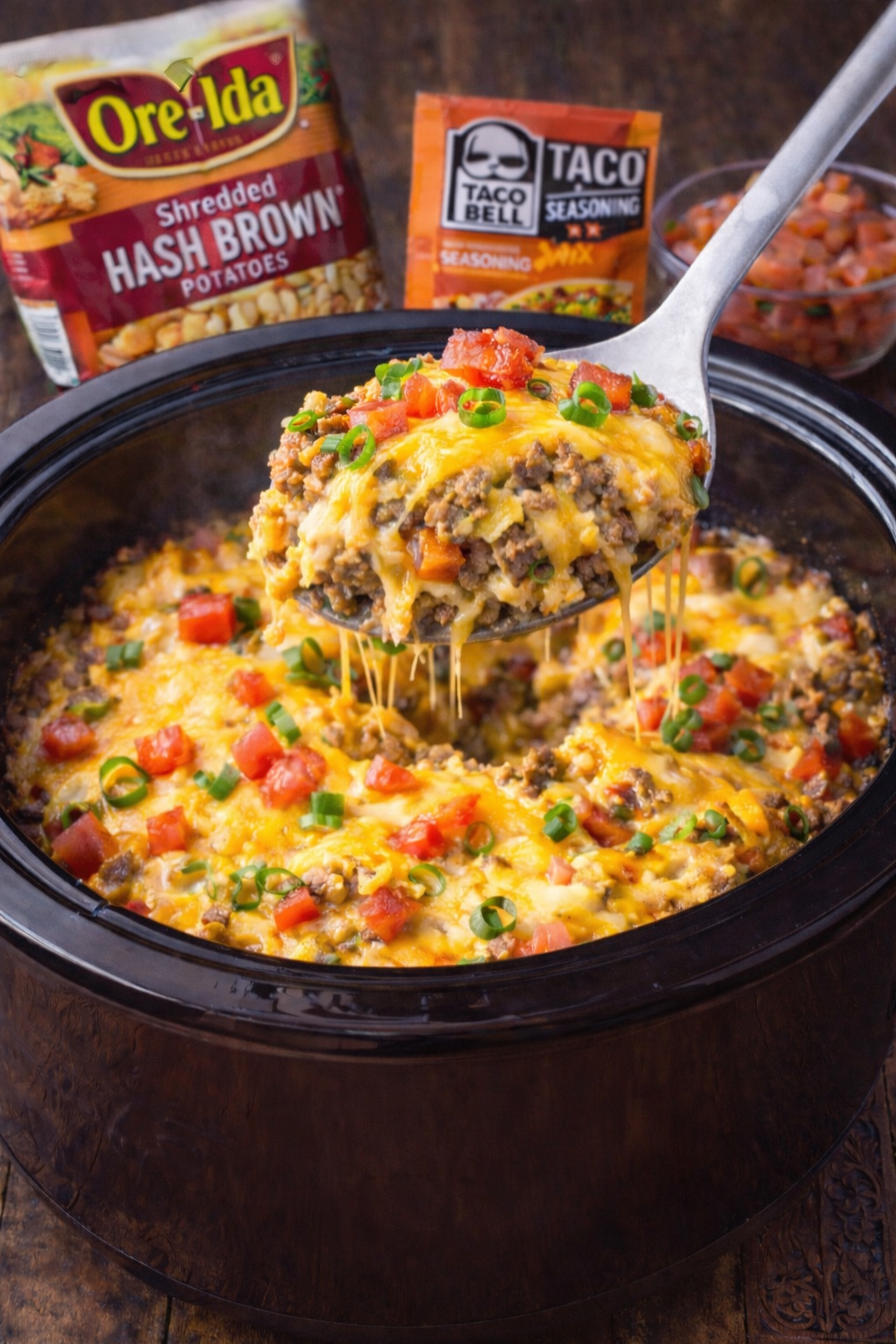 Slow Cooker John Wayne Casserole  in a black crockpot with a spoon lifting some up