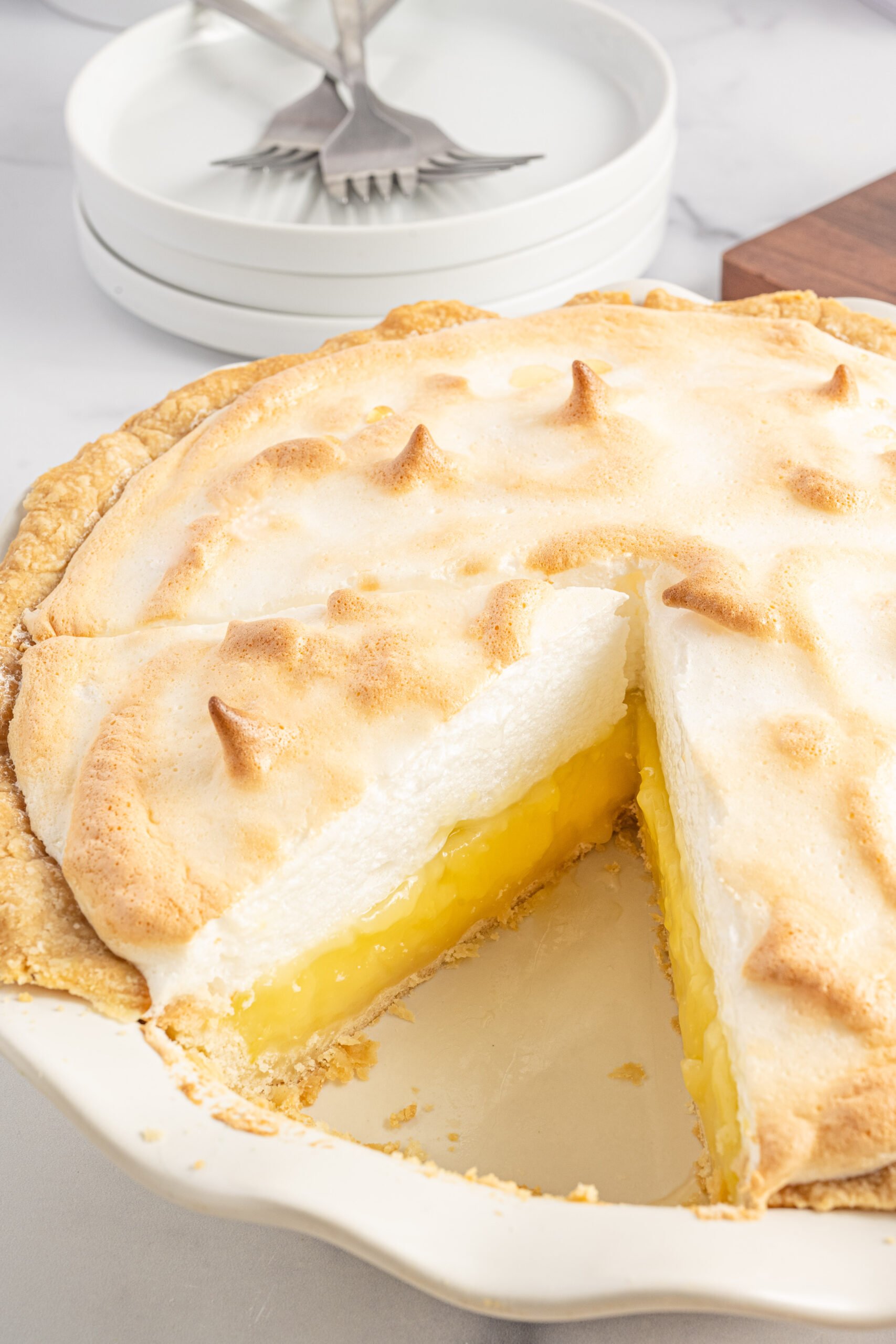 Side shot of a slice of lemon meringue pie in a white pie dish. 