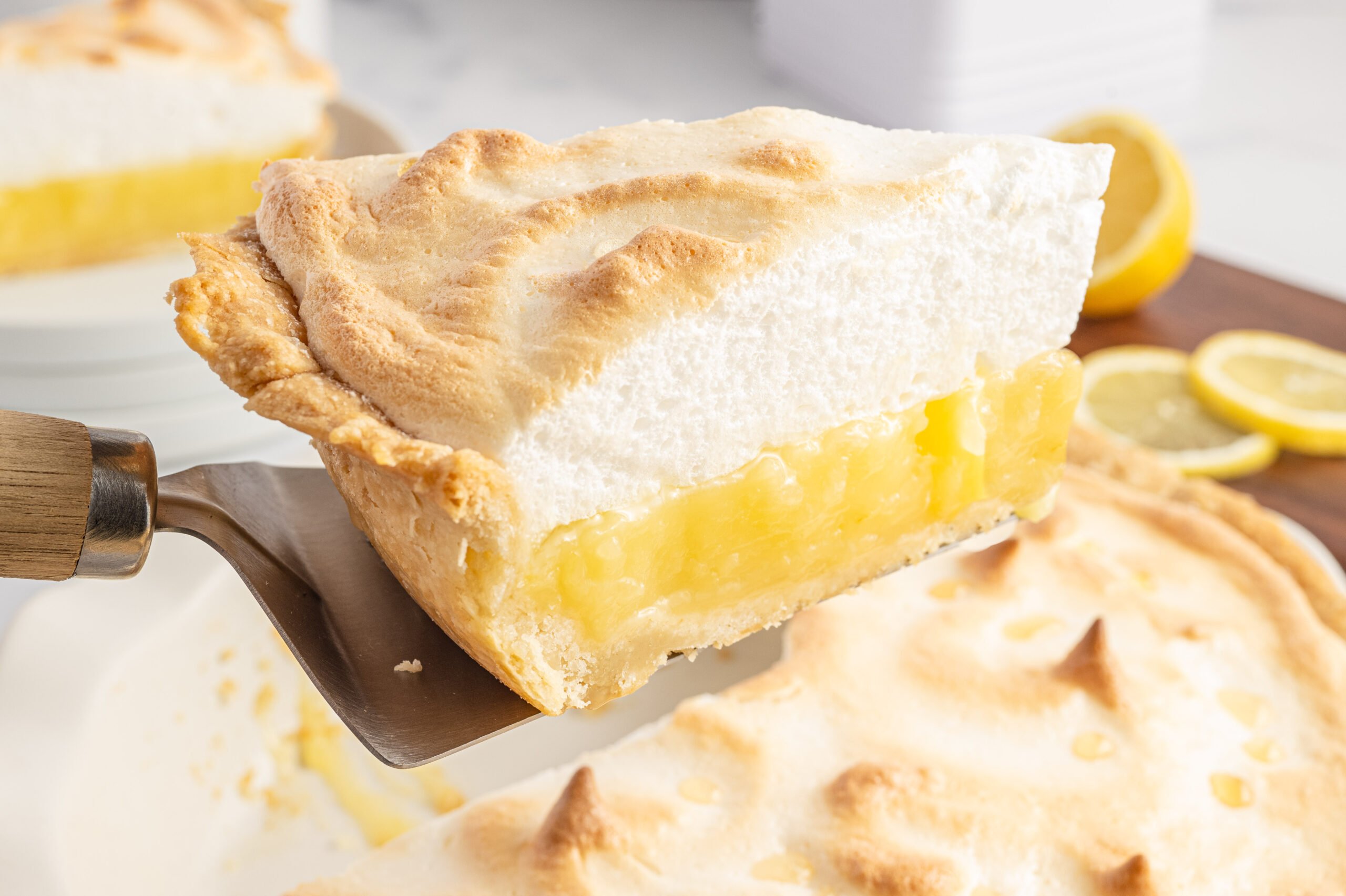 A slice of lemon pie being held up by a silver and wooden spatula. 