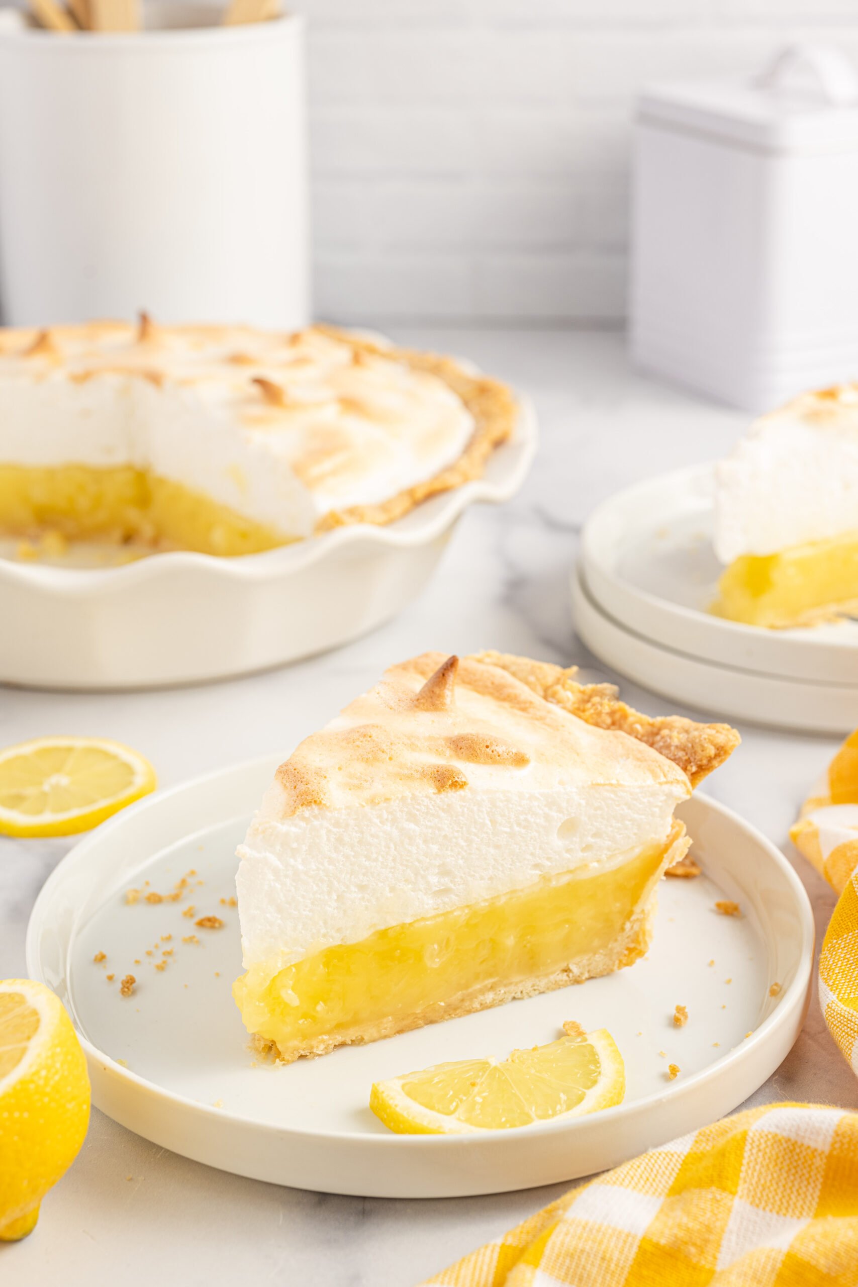 up close view of a piece of the lemon meringue pie on a white plate with fresh sliced lemons. 