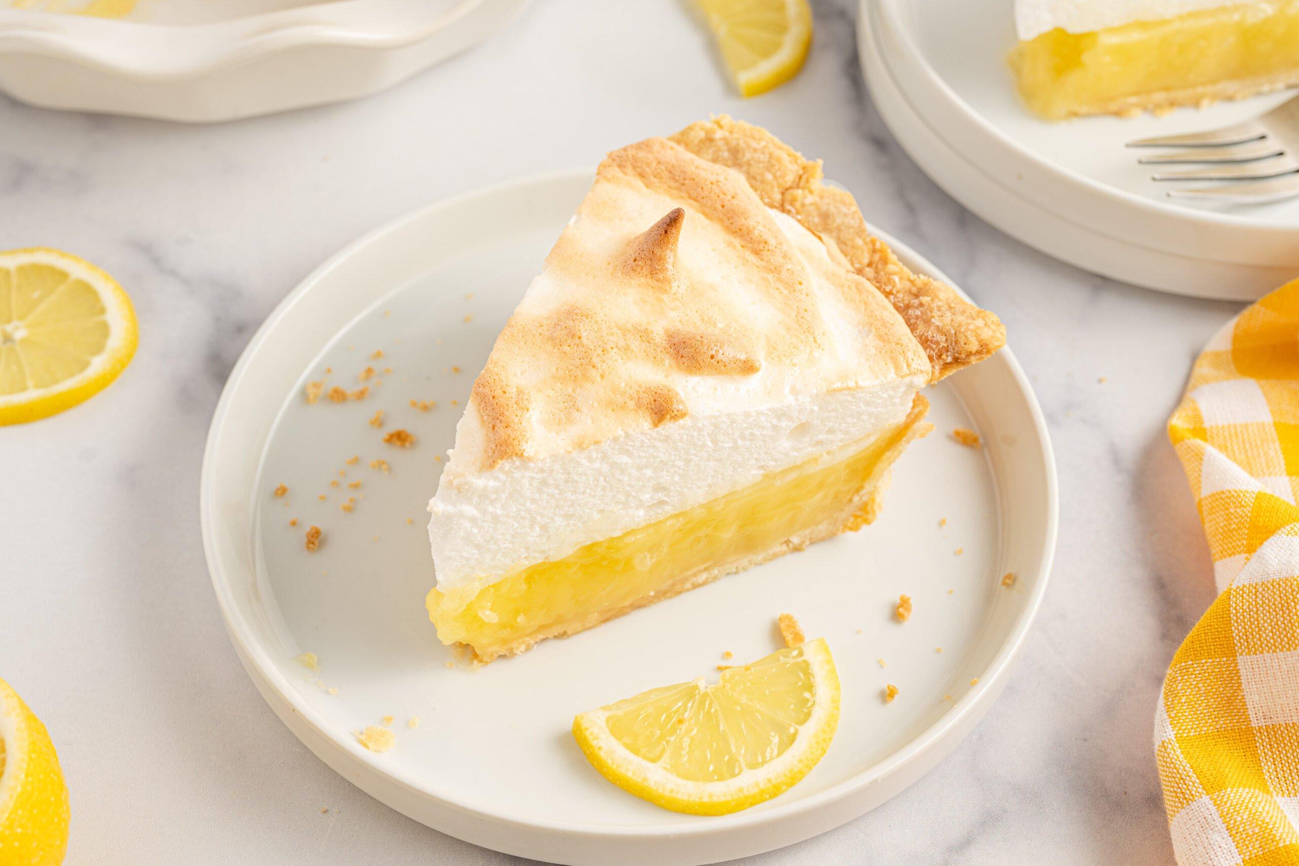 A piece of meringue pie on a white plate with fresh lemons. 