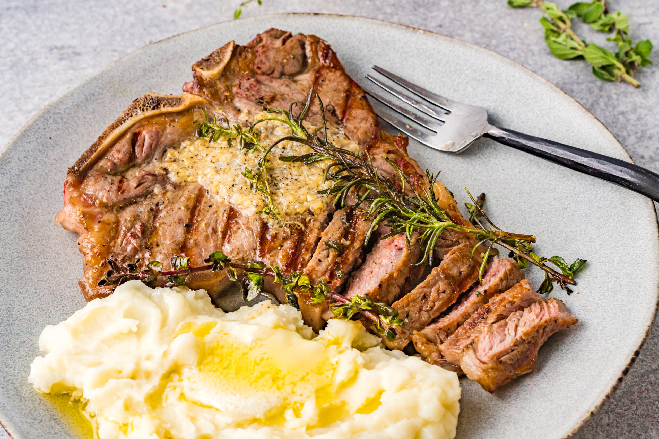 Overhead view of T Bone Steak on a white plate served with mashed potatoes.